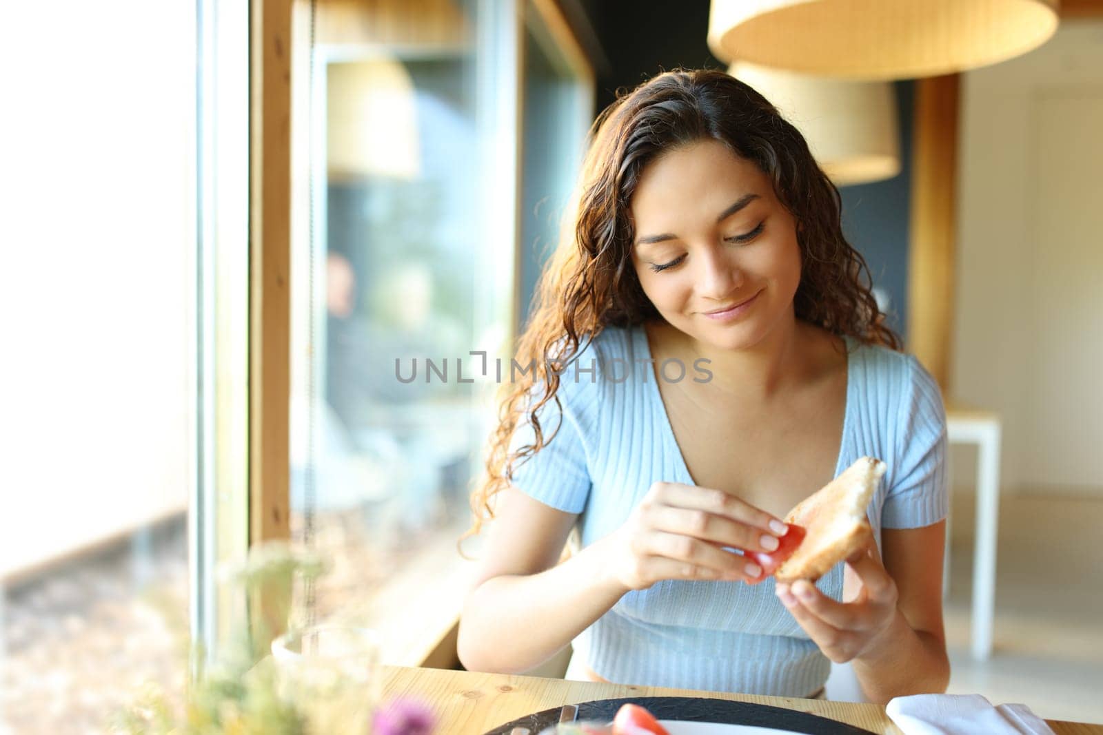 Front view of a happy woman spreading tomato on bread sitting in a restaurant