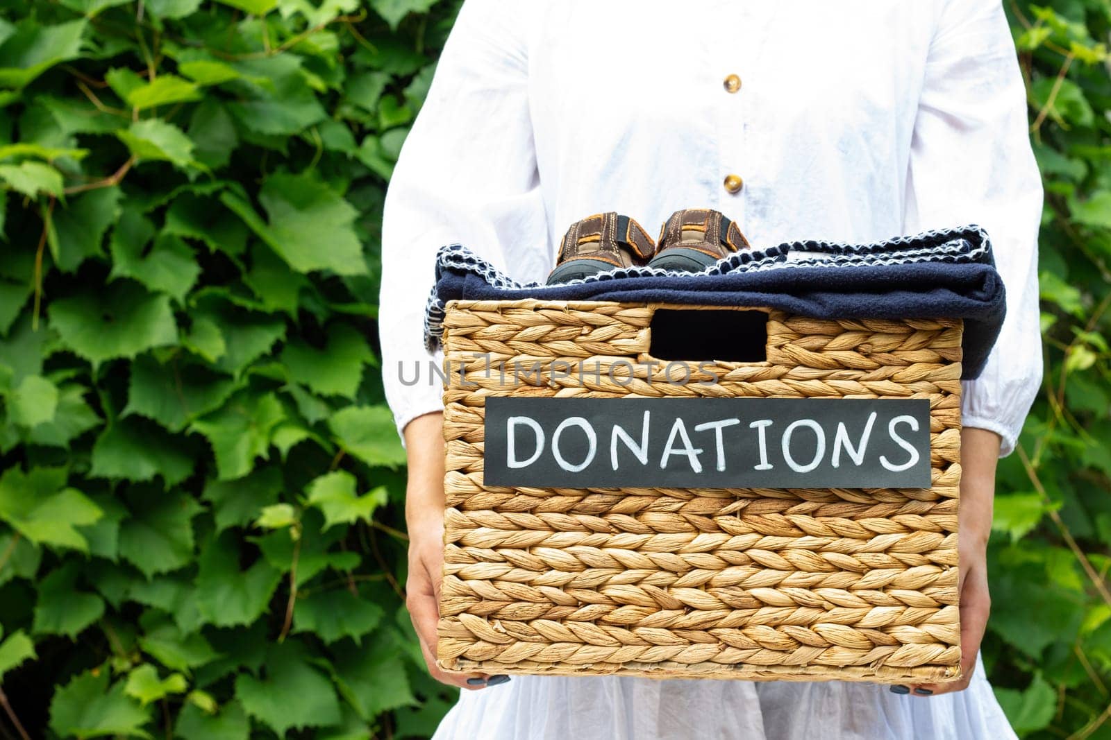 Female hands holding a box for clothing donations on a greenery background. Charity and donation concept, copy space.