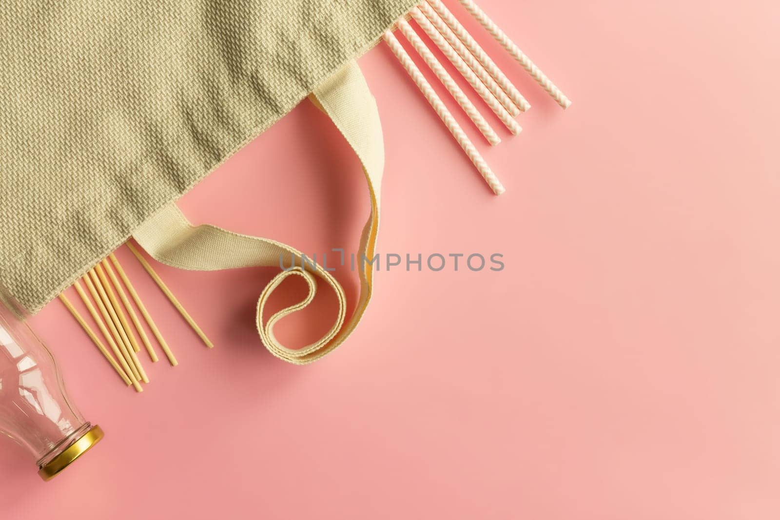 Fabric cotton shopping bags, glass bottles and jars, paper straws and wooden sticks on a pink background. Zero waste and ecological concept. Top view. Copy space.