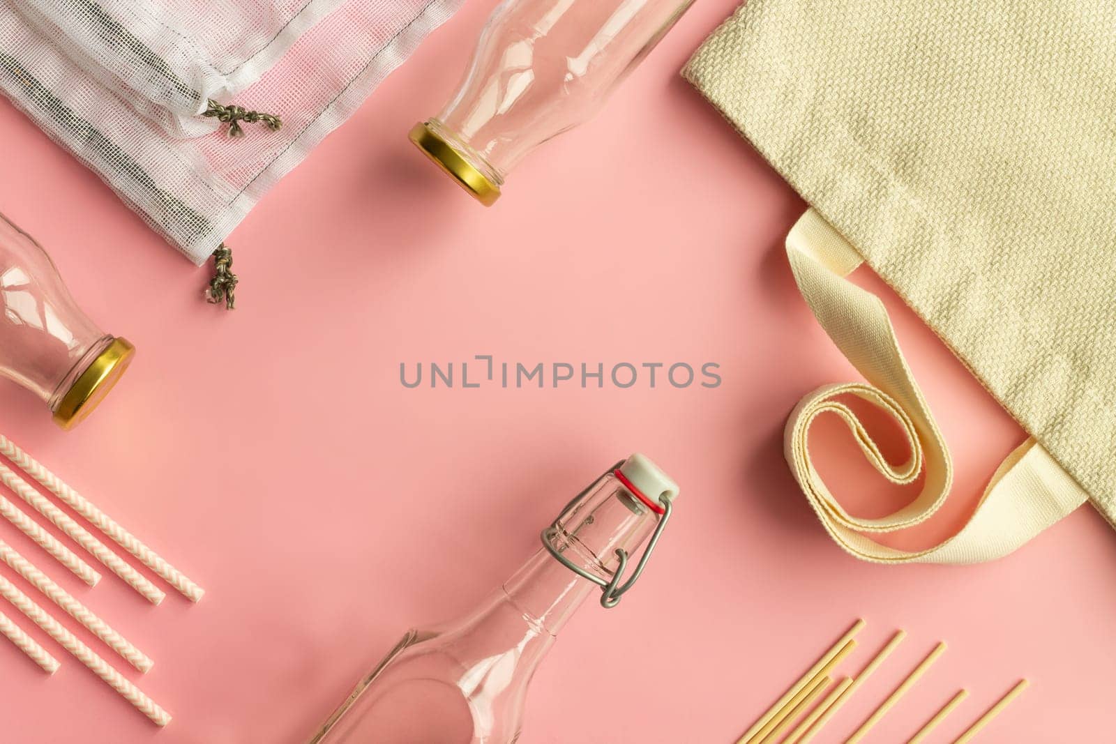 Fabric cotton shopping bags, glass bottles and jars, paper straws and wooden sticks on a pink background. Zero waste and ecological concept. Top view. Copy space.