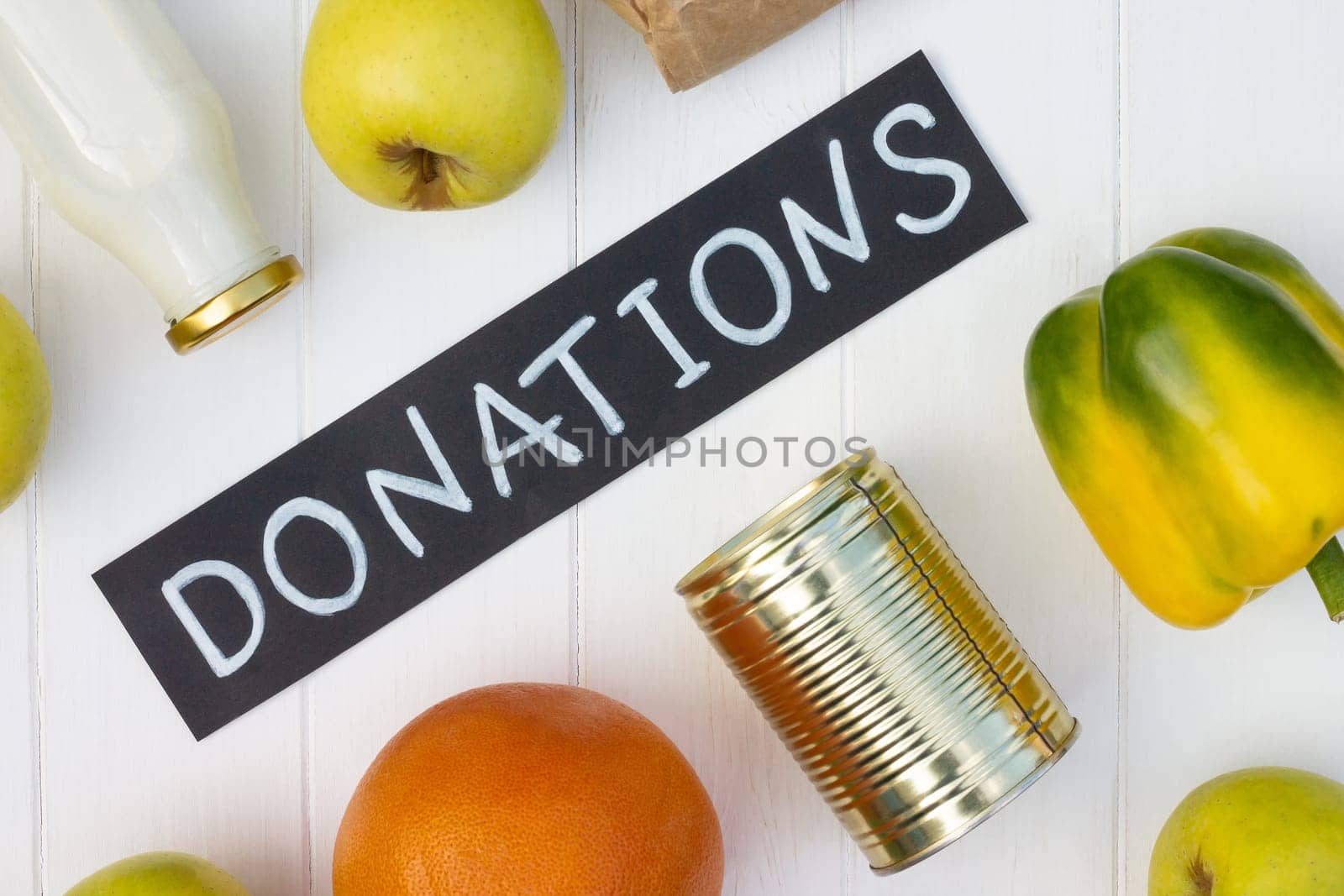 Cereals, canned food, milk, vegetables and fruits with a chalk Donations sign on a white wooden table. Flat lay. Charity and donation concept.