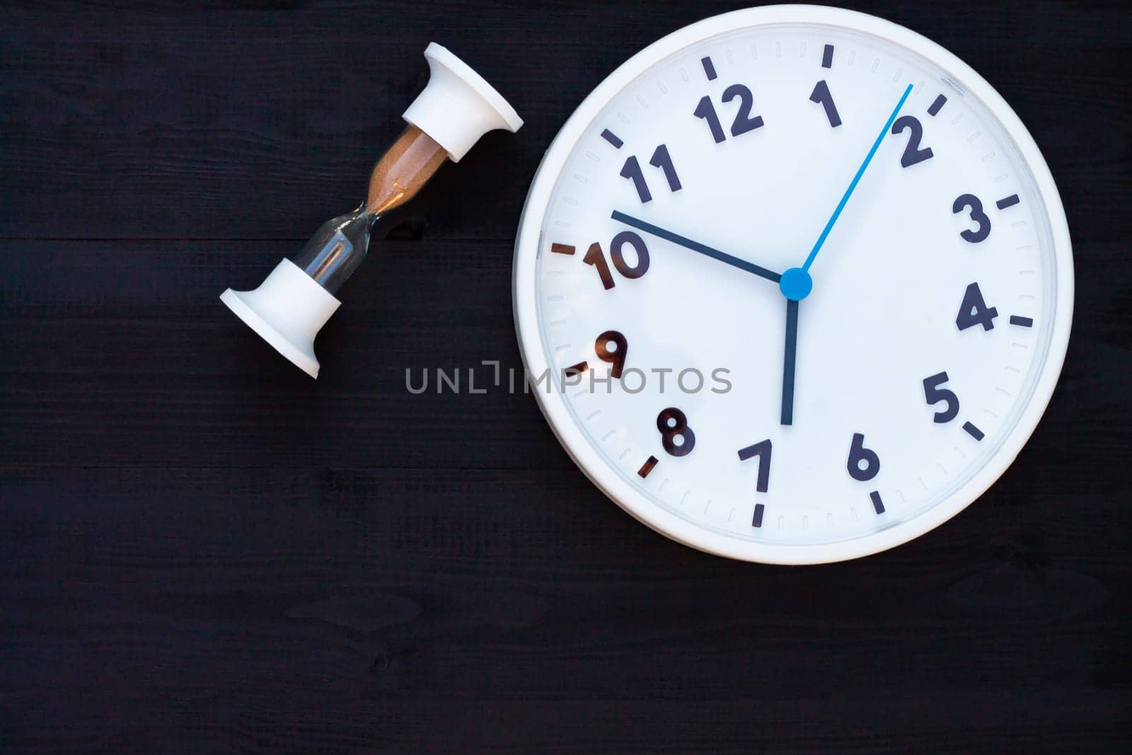 White clock and hourglass on a black wooden background. Top view. Copy space. Education or business concept.