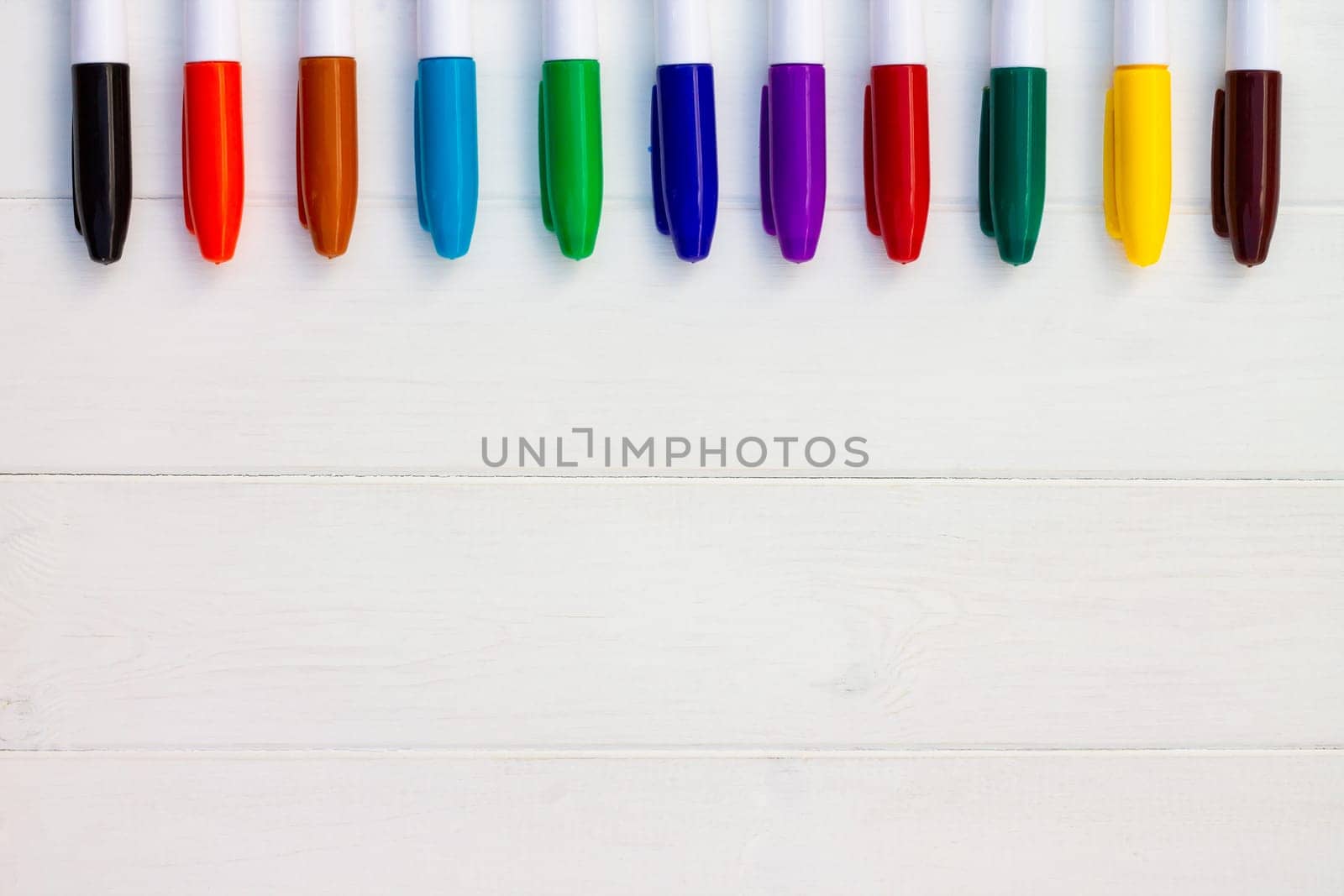 Multi-colored markers on a white wooden background. Top view. Copy space