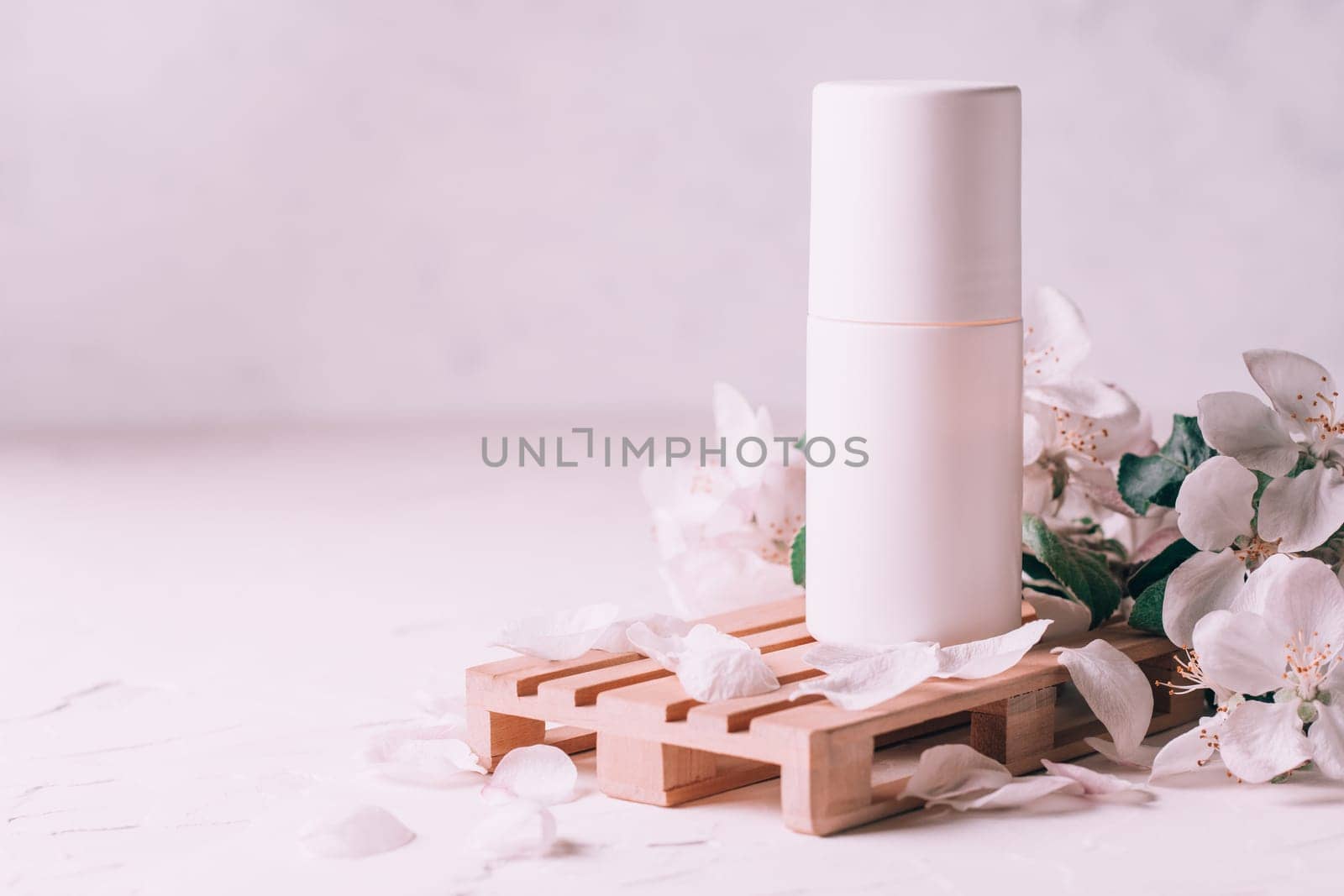 Antiperspirant roll-on deodorant on wooden podium in form of pallet on light plaster surface with apple flowers. Copy space