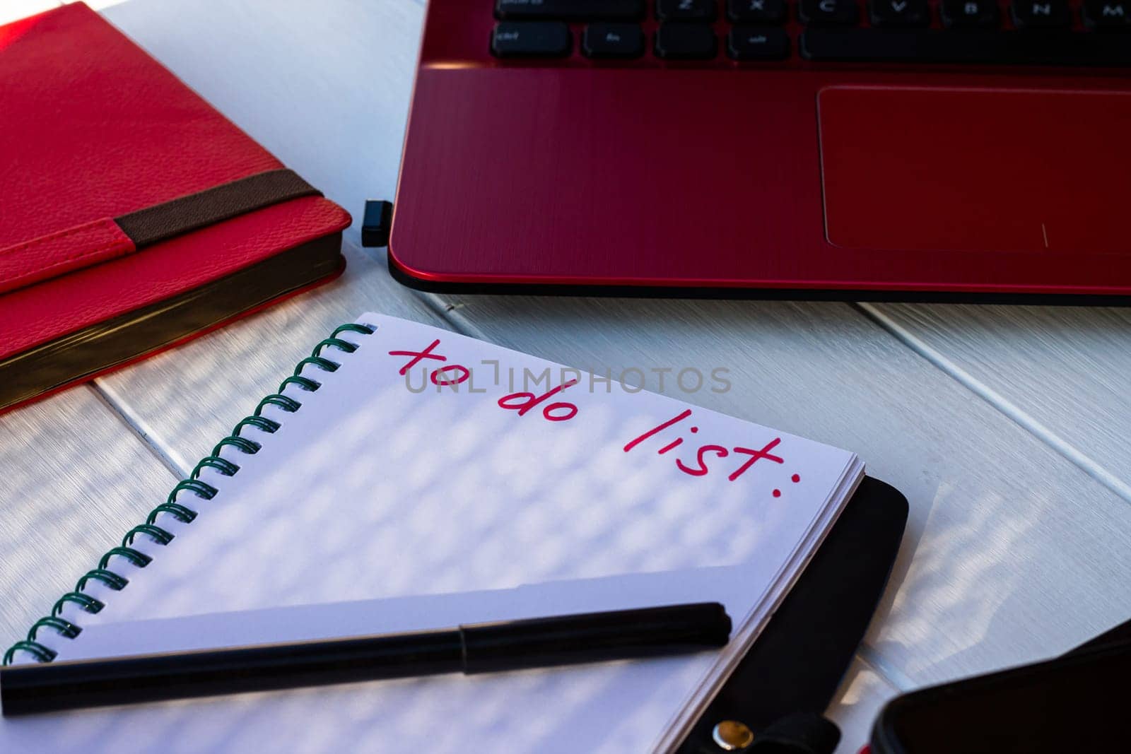 Notebook with To Do List with phone, red diary and laptop on a white wooden background