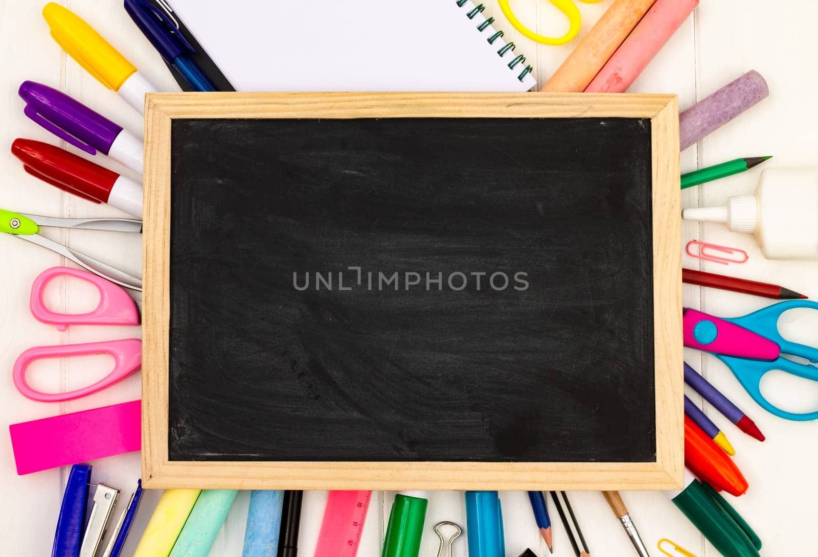 Back to school black chalk board on a white wooden background, color supplies. Top view. Copy space. Education concept