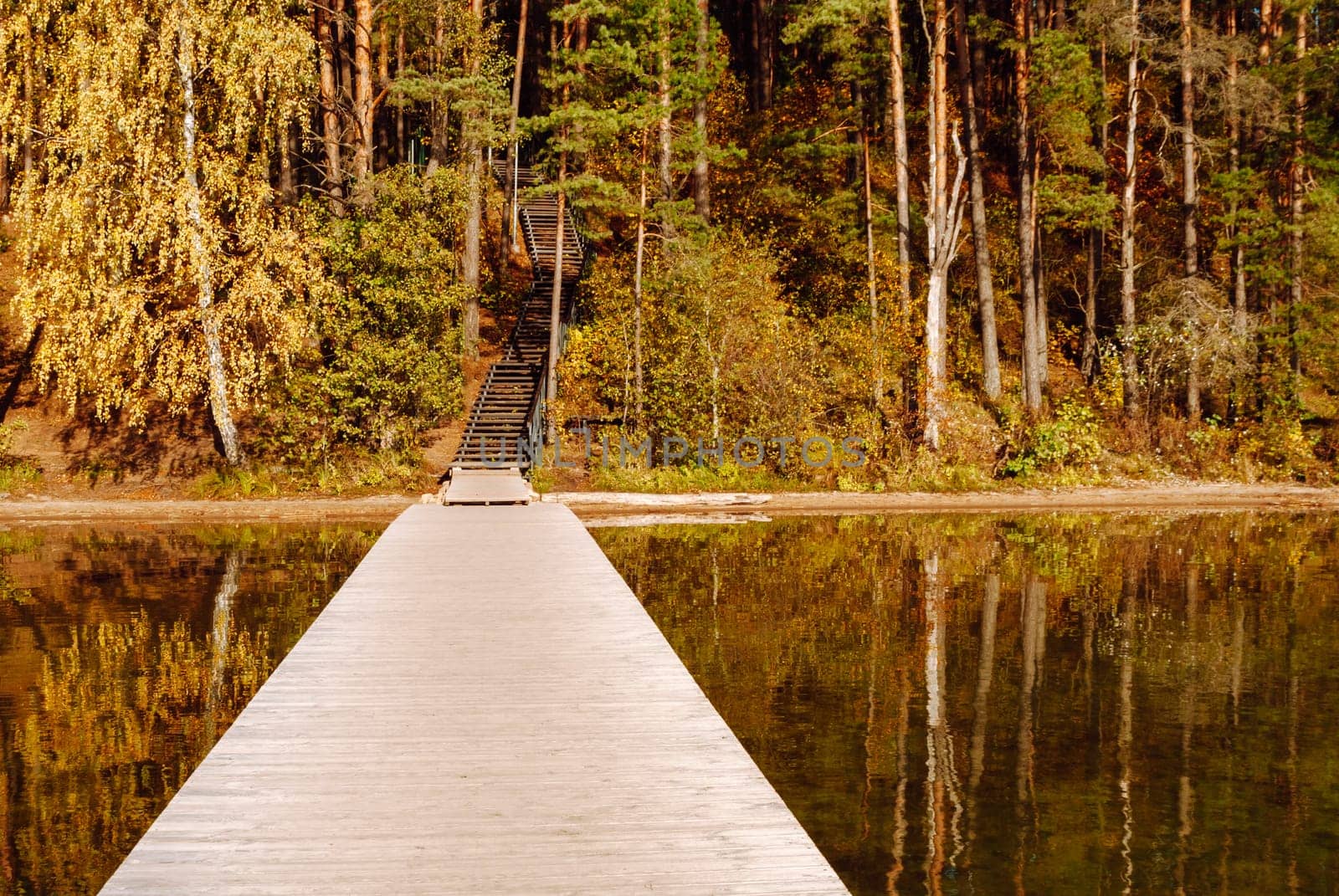 Wooden pier, autumn forest and wooden stairs up to a hill on Lake Baltieji Lakajai in Labanoras Regional Park, Lithuania.