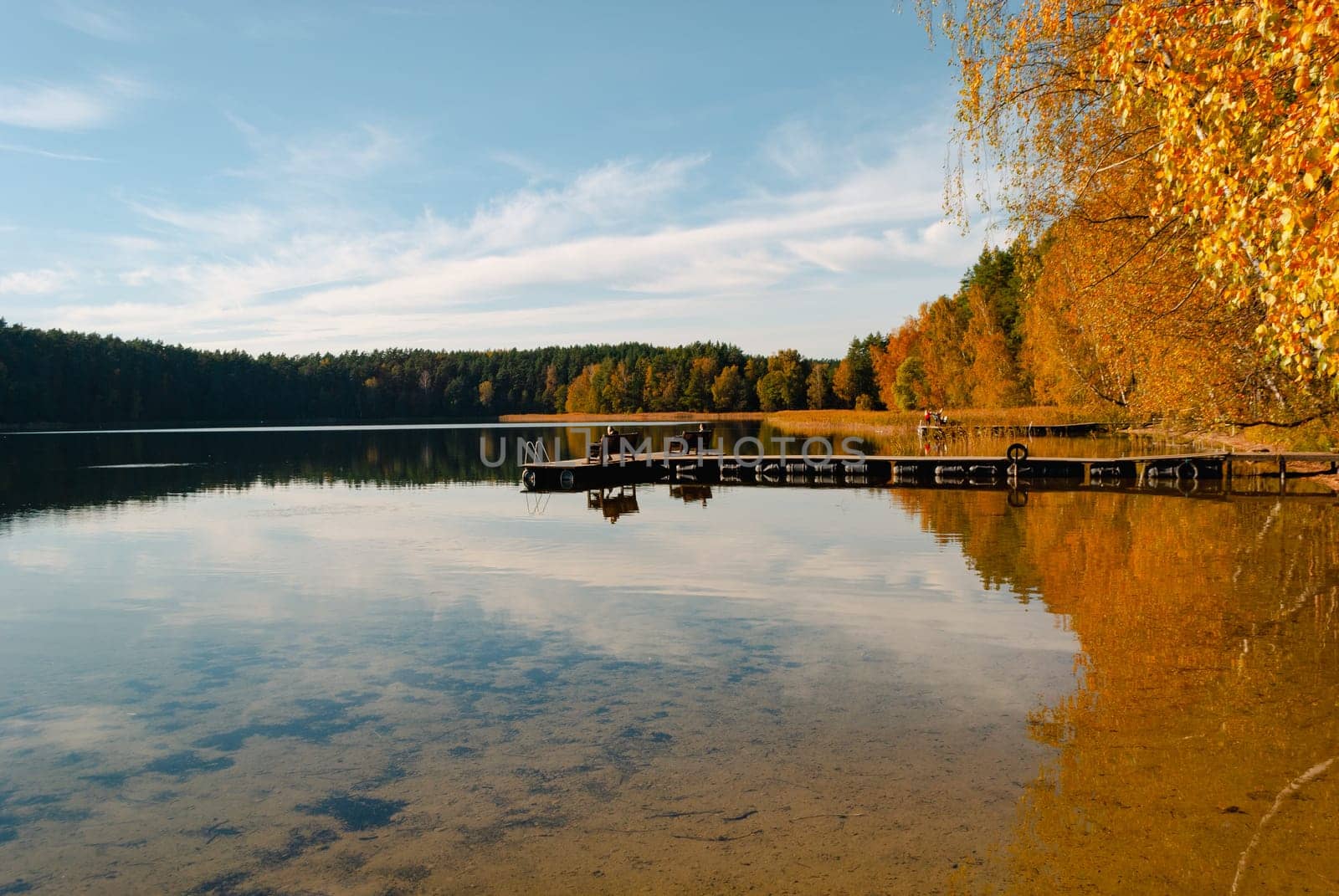 Lake Baltieji Lakajai with clear water in Labanoras Regional Park and a wooden marina with benches for relaxation. Autumn trees are covered in the water
