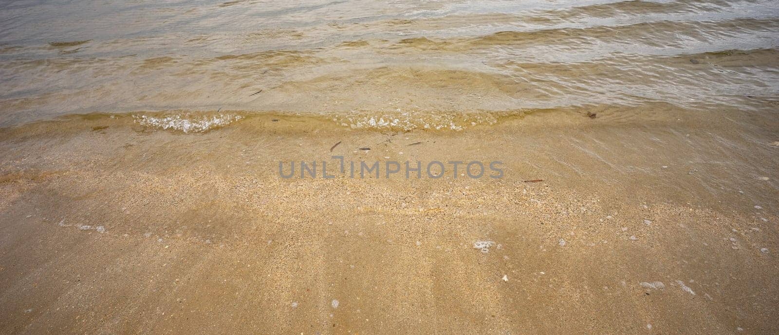 Clear sea water and small waves and ripples crossing a sandy beach and shellgrit as the tide comes in on the foreshores of Hervey bay, Queensland.