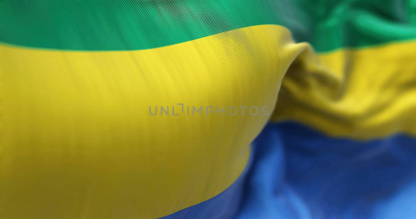 Close-up view of the Gabon national flag waving in the wind. The Gabonese Republic is a Central African Country. Fabric textured background. Selective focus