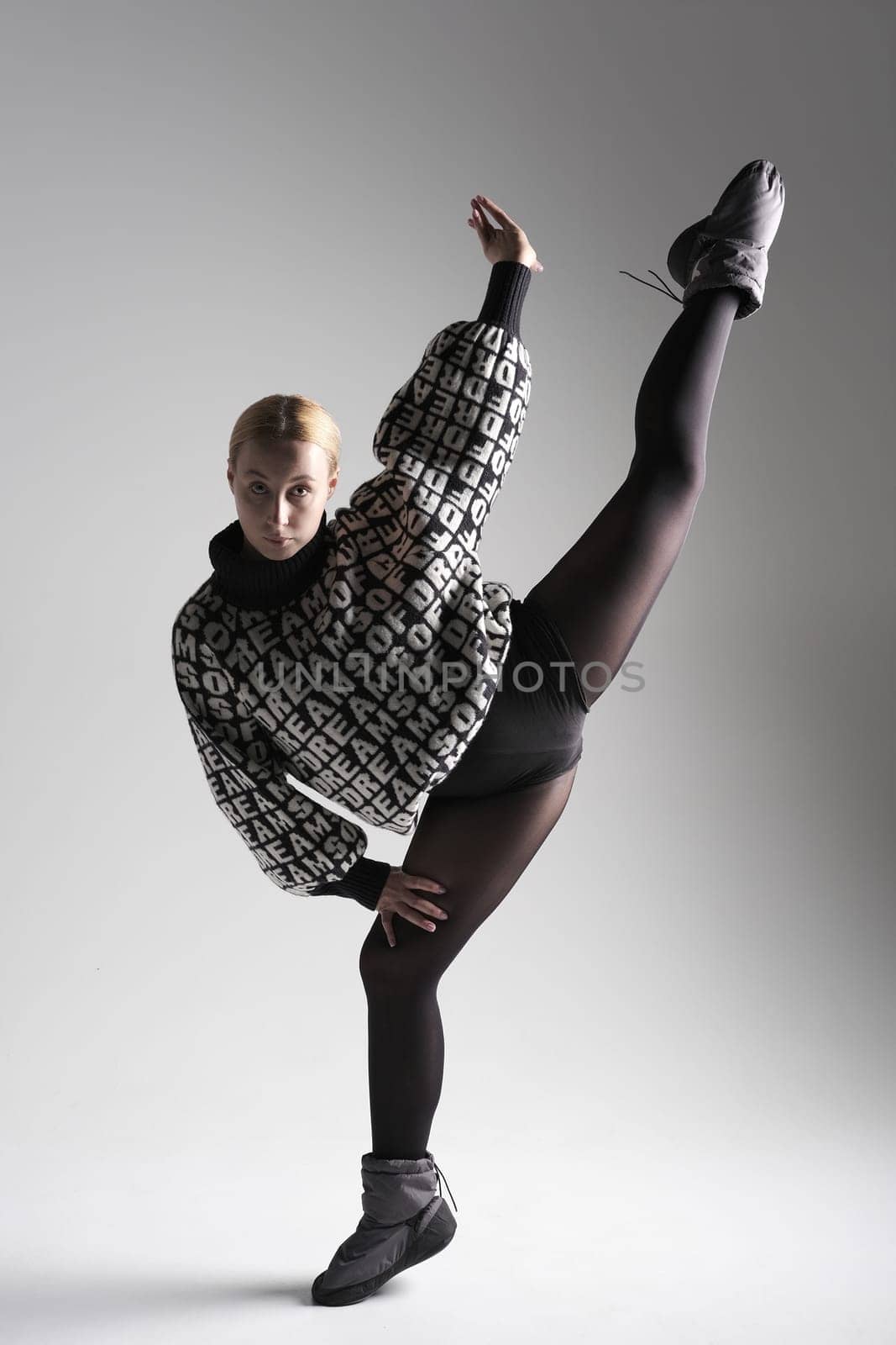 Ballet dancer woman black dress on gray background, Ballerina posing and showing her flexibility on gray background in studio. With text on sweater DREAMS OF.