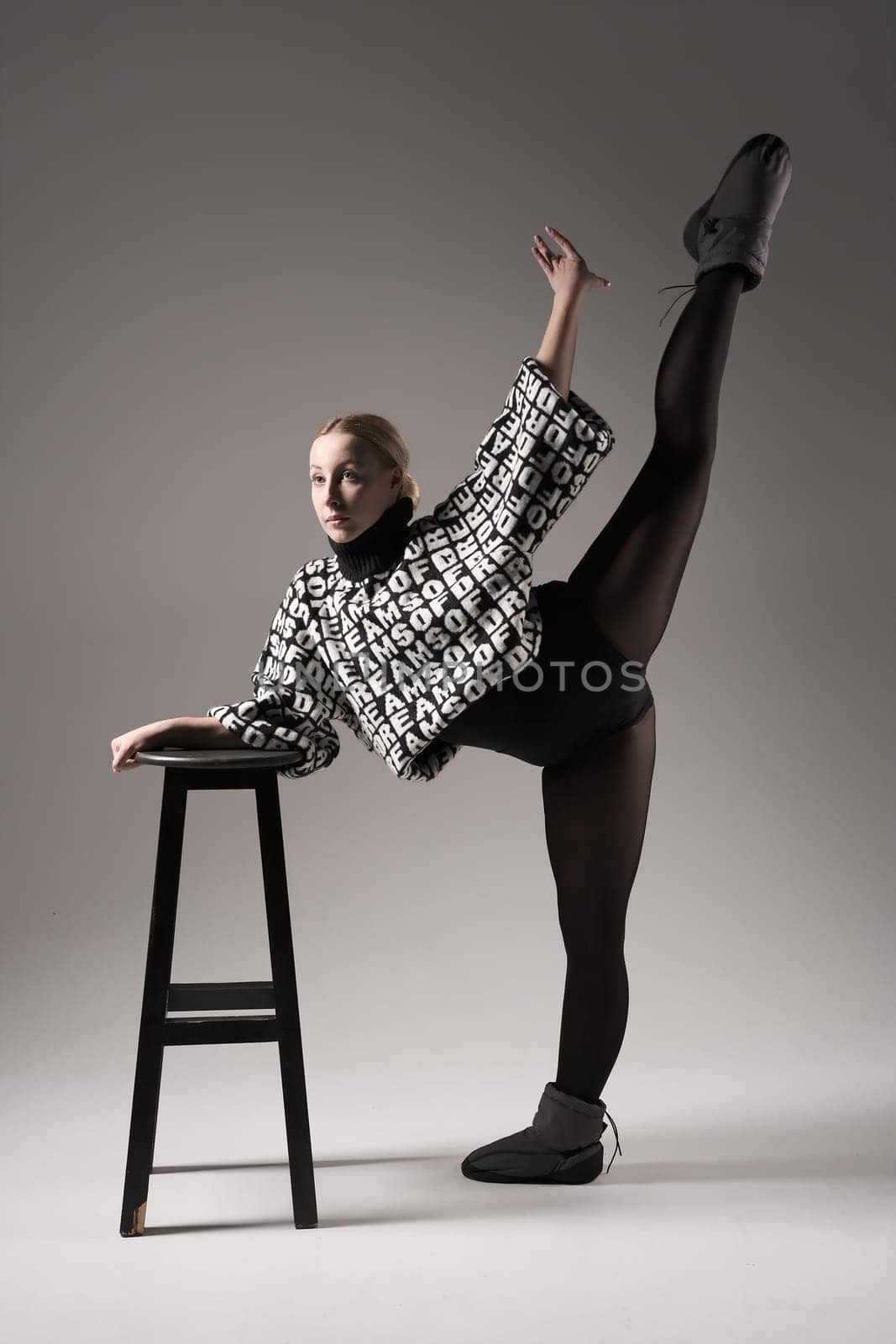 Ballet dancer woman black dress on gray background, Ballerina posing and showing her flexibility on gray background in studio with chair. Text on sweater DREAMS OF.