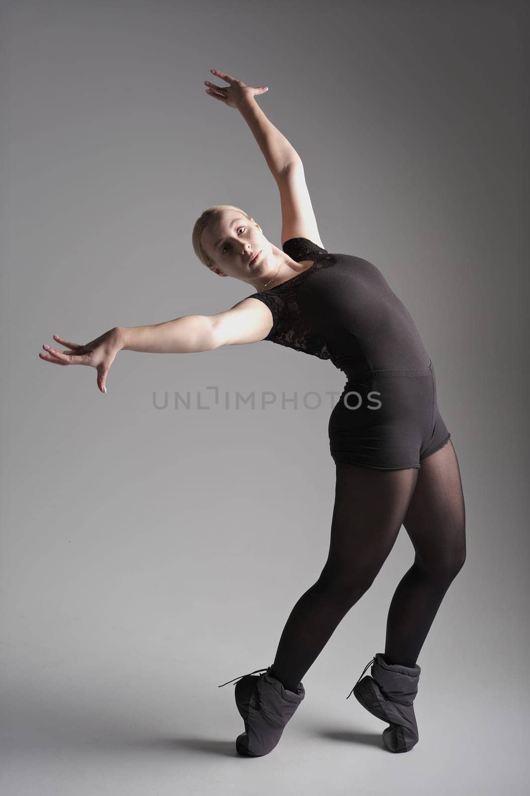 Ballet dancer woman black dress on gray background, Ballerina posing and showing her flexibility on gray background in studio.