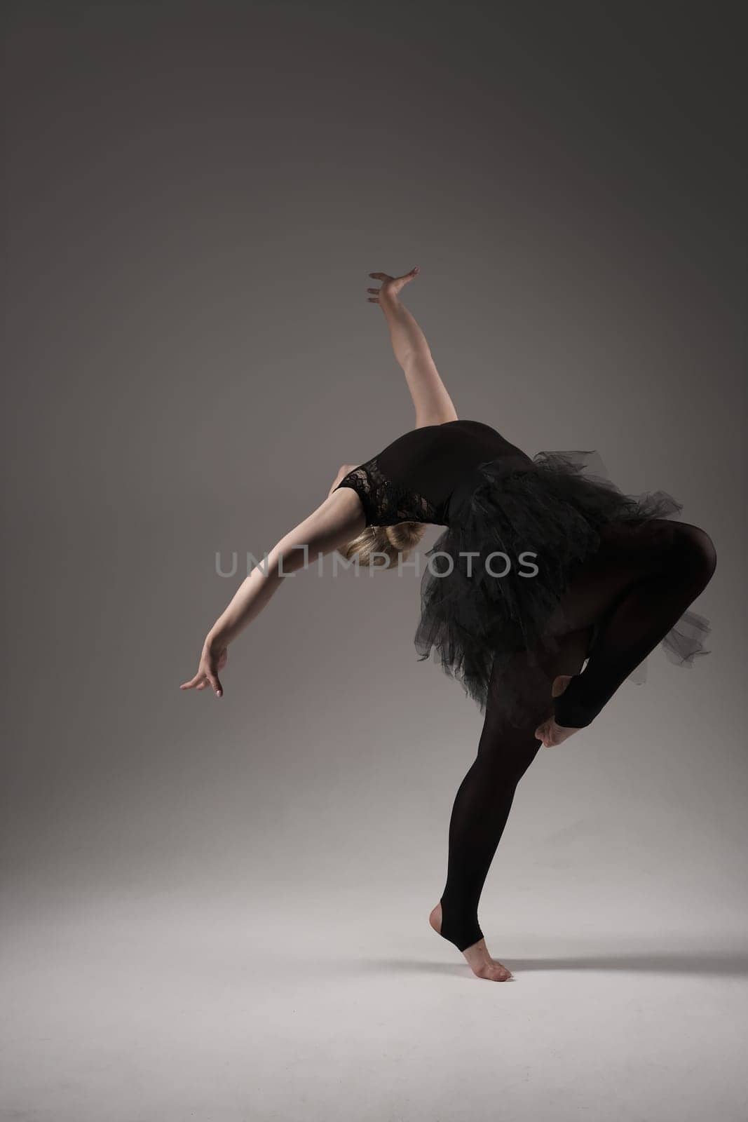 Ballerina Dancing with tutu Modern Ballet Dancer in dancer tutu, Gray Background. Dancer in Black clothes showing her flexibility posing on gray background in studio.