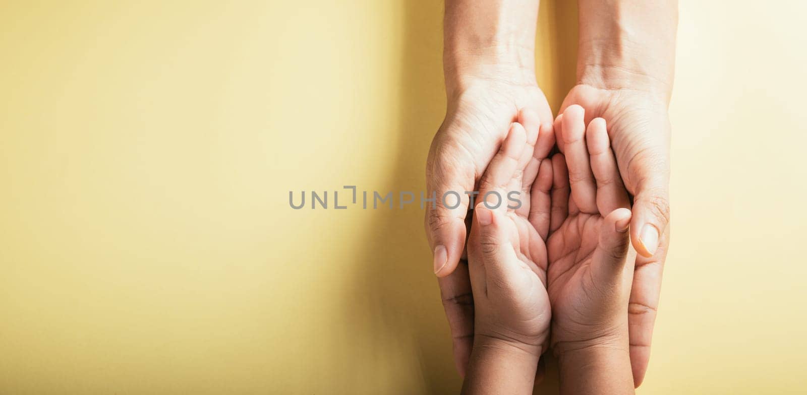 Top view parents and little kid holding empty hands together studio shot isolated on yellow background, family home, hands children on adult mother hand, help support, parents family day concept