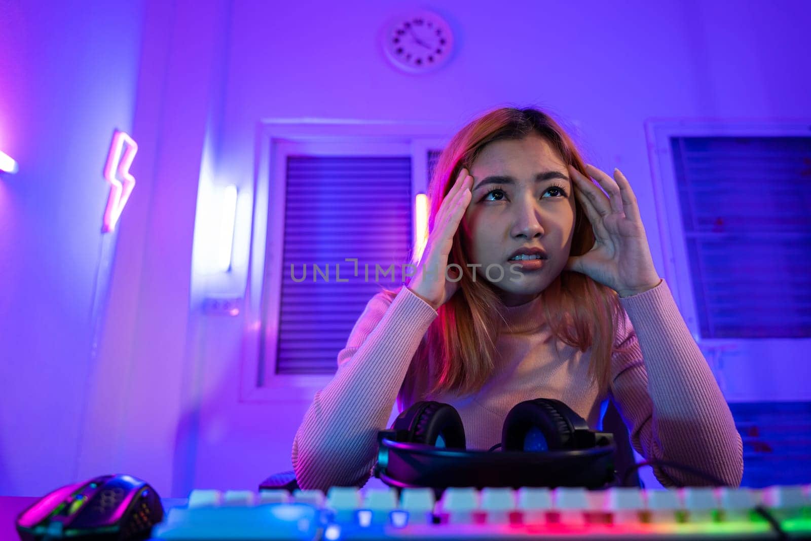 Game Over. Asian gamer playing online video game she losing and sad on computer PC colorful neon LED lights, young woman in gaming headphones feeling disappointed about lost game, E-Sport concept