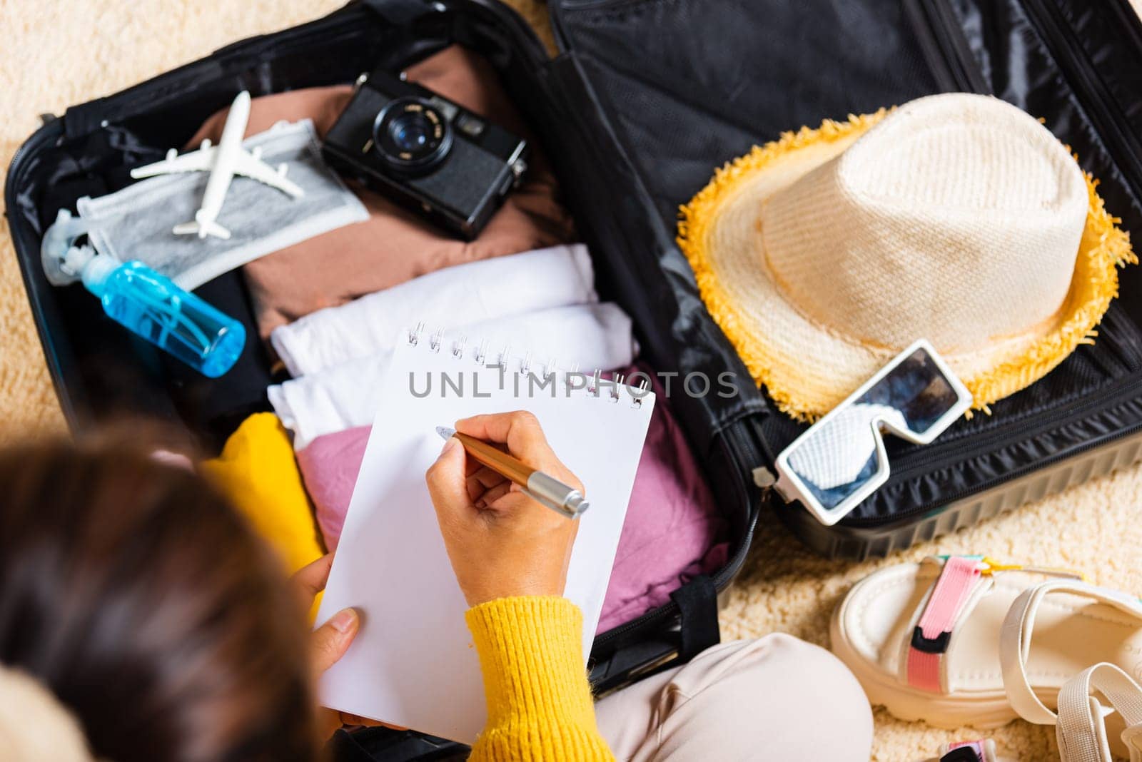 Making check list of things to pack for travel. Woman writing paper take note and packing suitcase to vacation writing paper list sitting on room, prepare clothes into luggage, Travel vacation travel