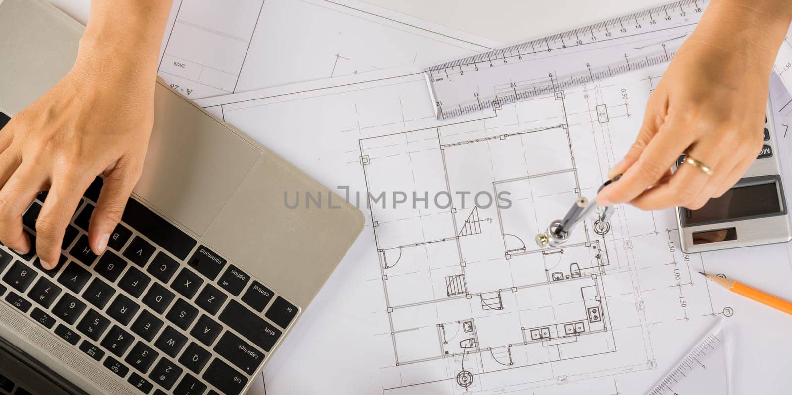 Architectural project workplace. Architect typing laptop keyboard to review design of house before editing or sketching with compass on plan blueprint paper on table desk at architecture office
