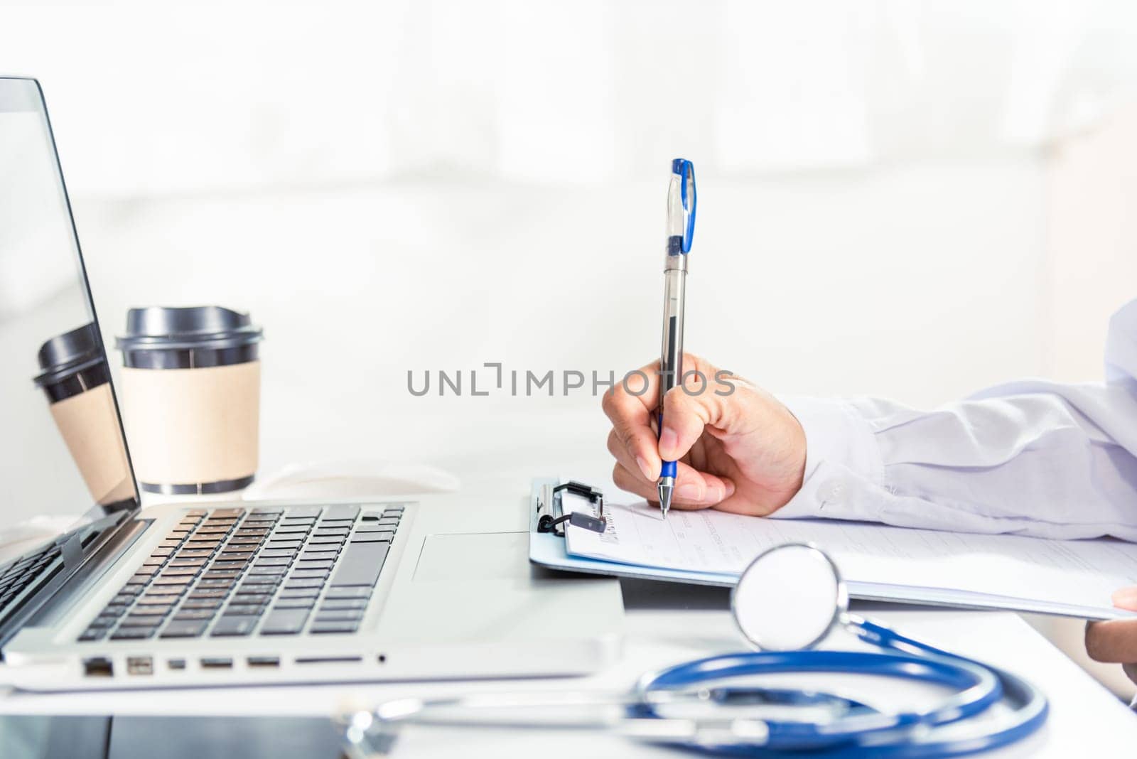 Doctor or nurse in uniform with stethoscope writing something information of patient prescription medical in paperwork checklist on clipboard on front laptop computer, medication history record