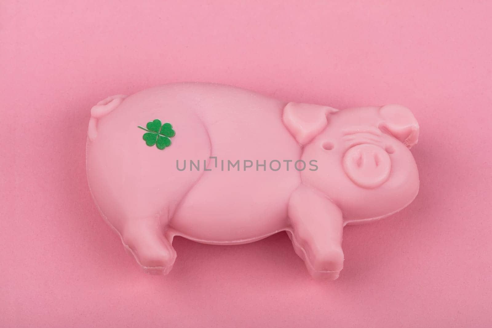 Piece of soap in shape of a Pig with shamrock from above over pink background.