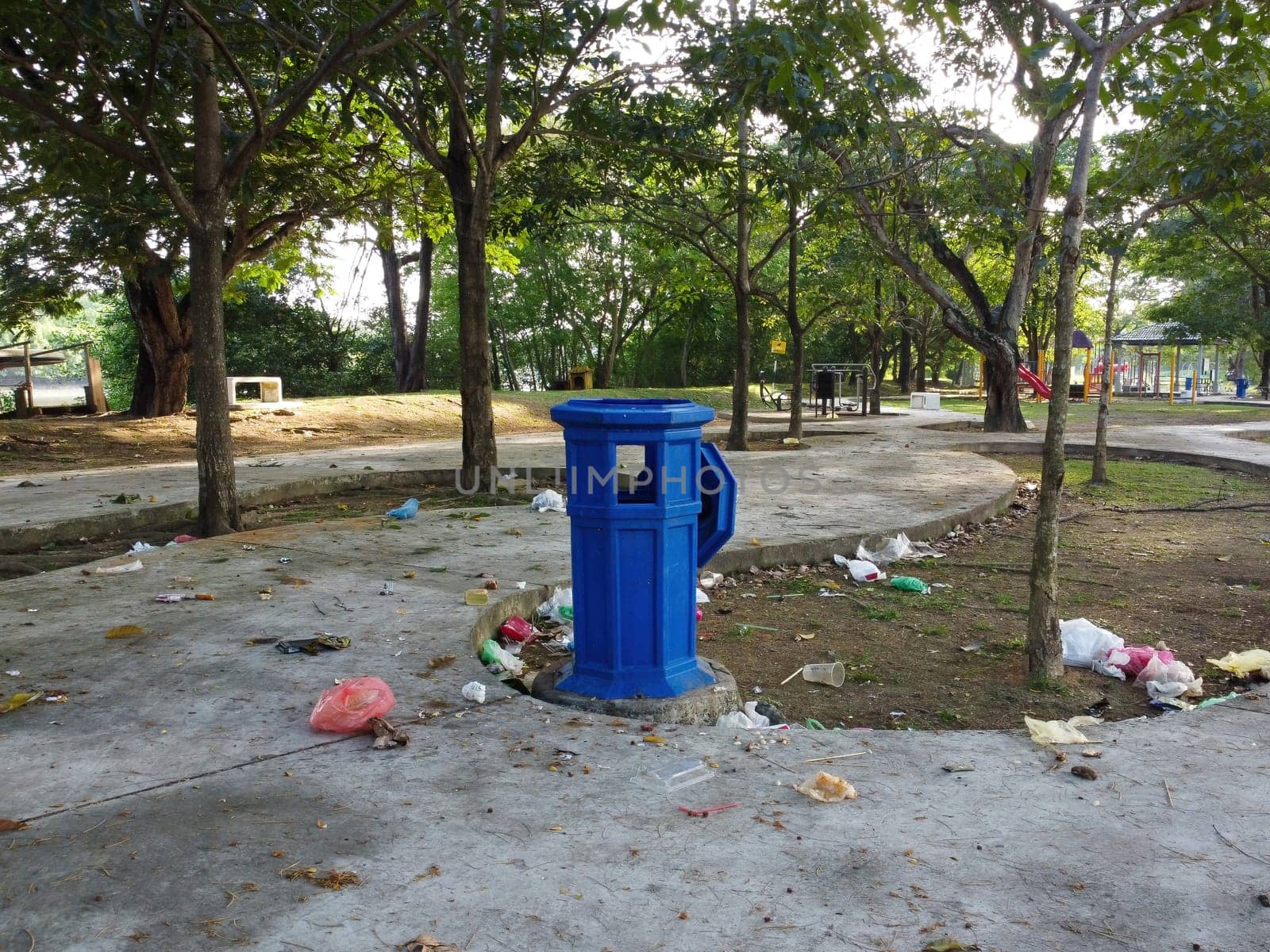 Blue dustbin and some garbage on floor at the park