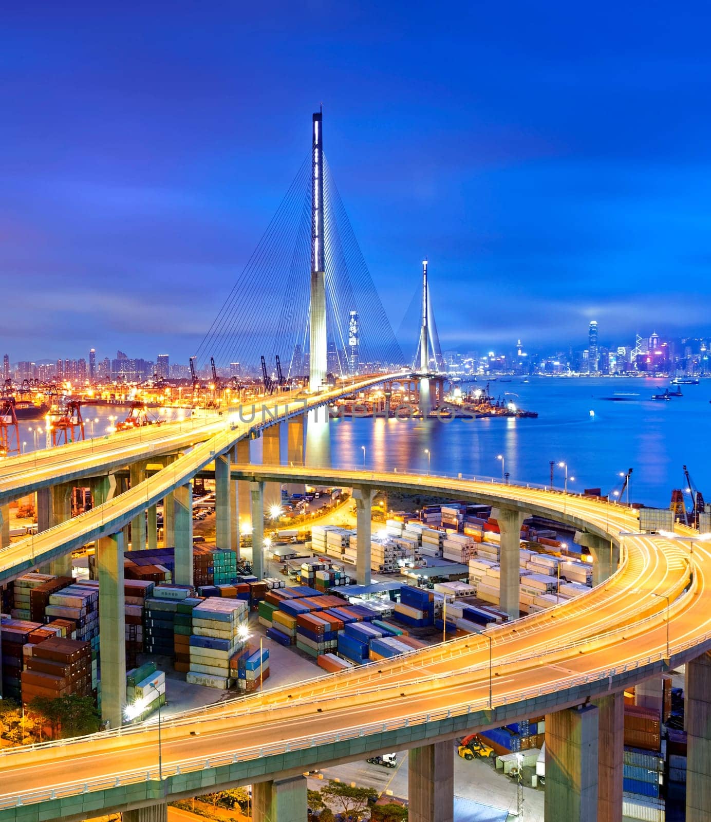 Container Cargo freight ship with working crane bridge in shipyard under Stonecutters highway bridge at sunset for Logistic Import Export, Hong kong