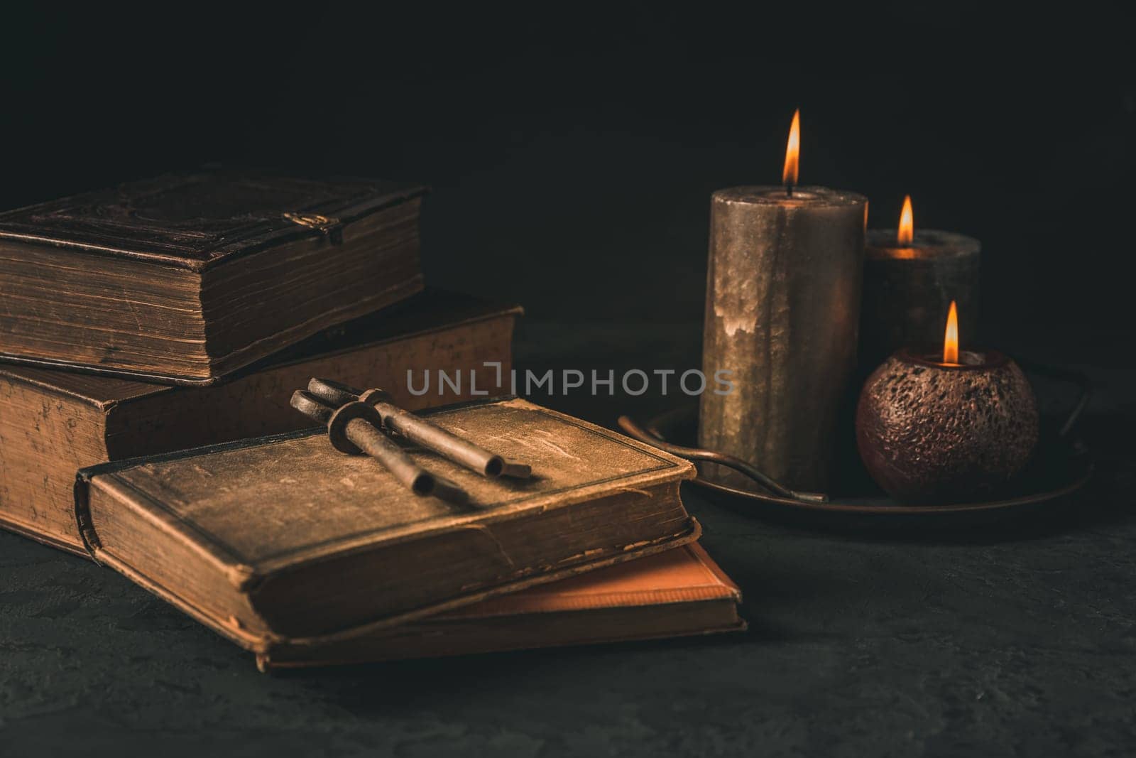 Pile of old antique books with candle and old rusty keys in vintage style on black background