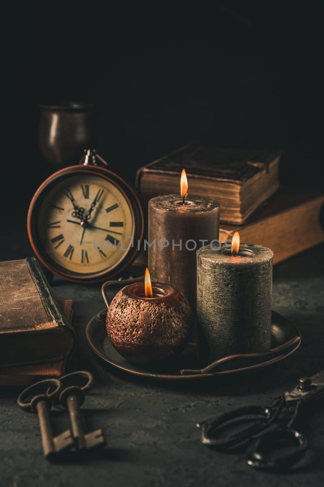 Candles, antique books, old clock and old rusty keys in vintage style on black background