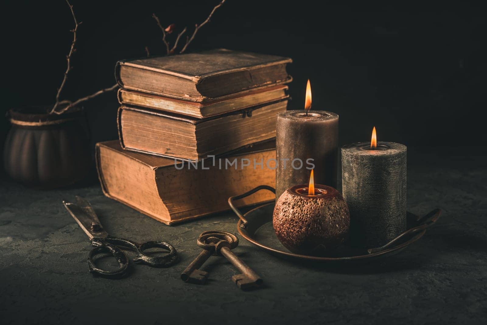 Pile of old antique books with candle and old rusty keys in vintage style on black background