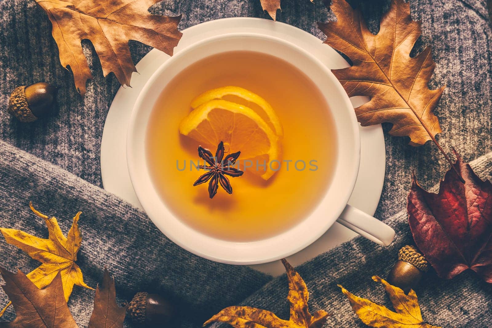 Hot lemon tea for cold season with warm sweater and autumn leaves