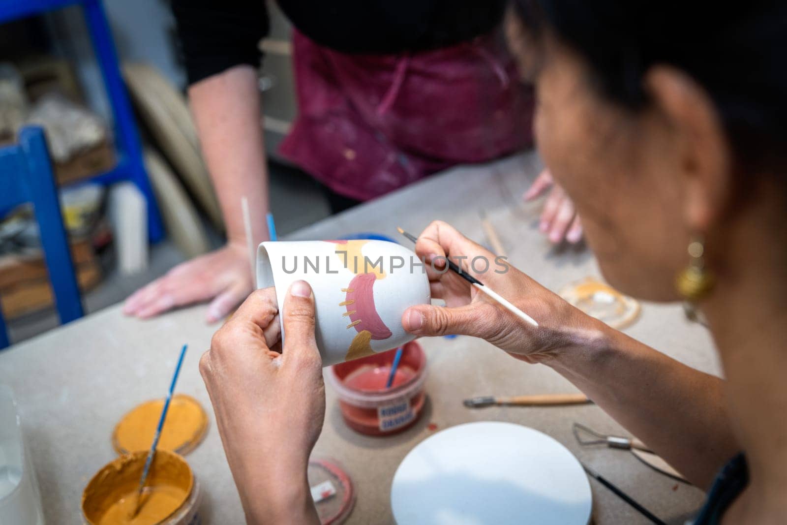 women's hands painting a pottery object