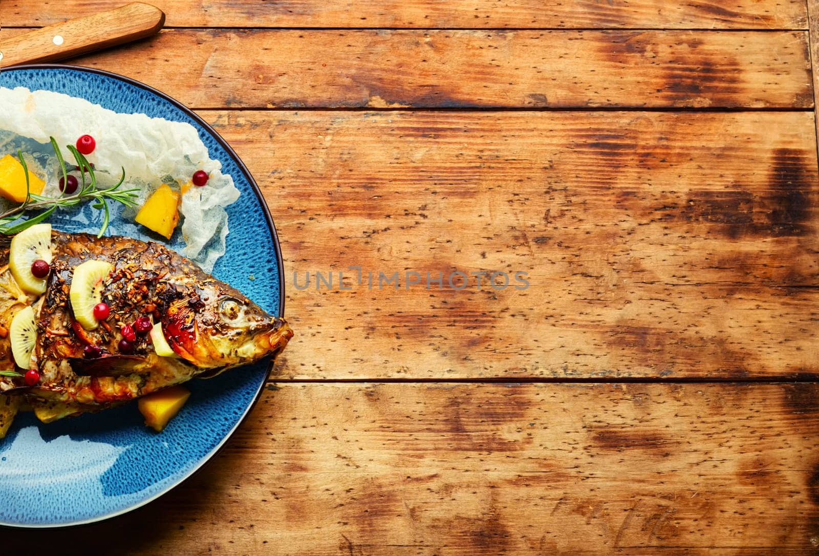 Tasty baked whole fish in fruit marinade on old wooden table