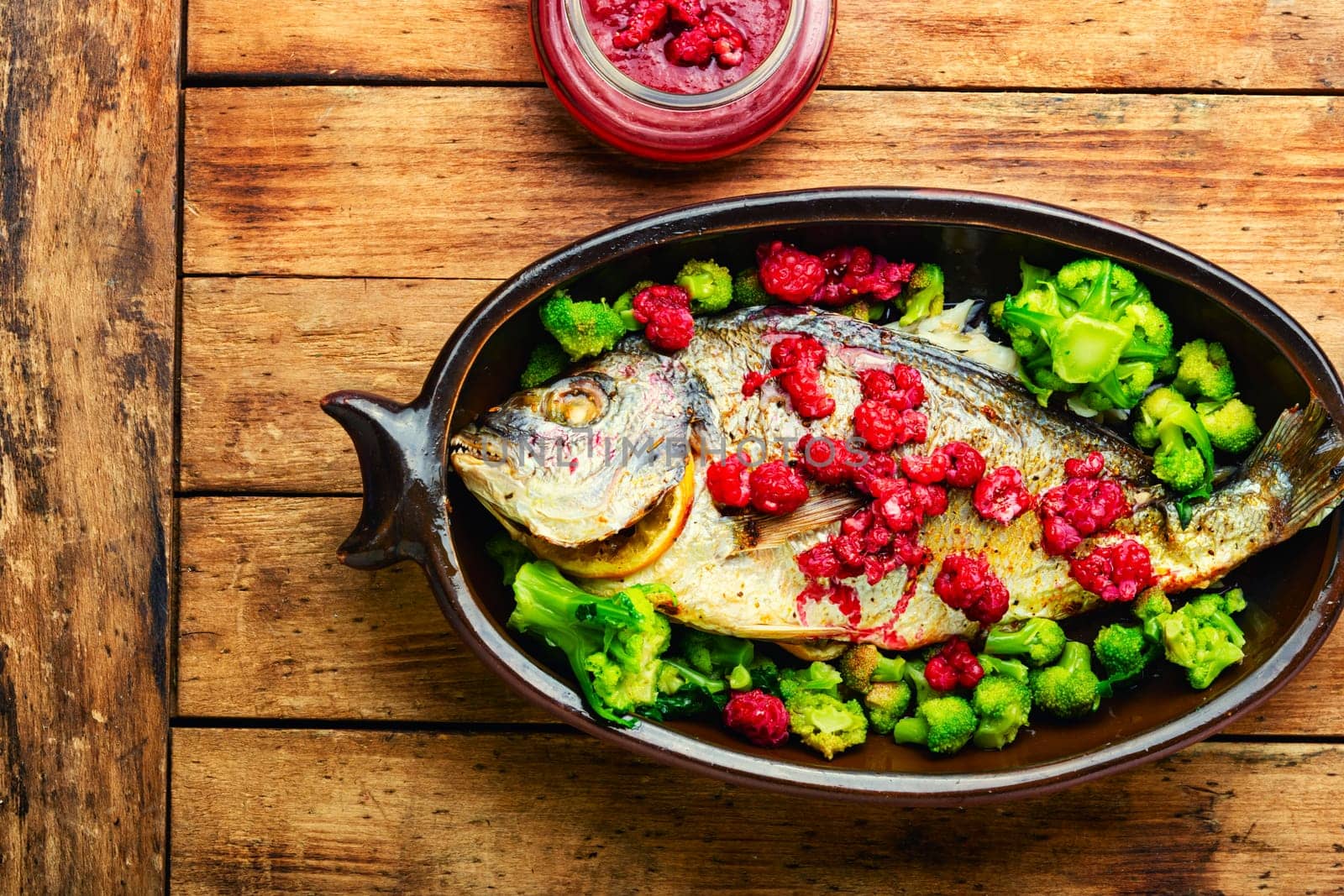 Tasty baked whole fish in fruit marinade on old wooden table