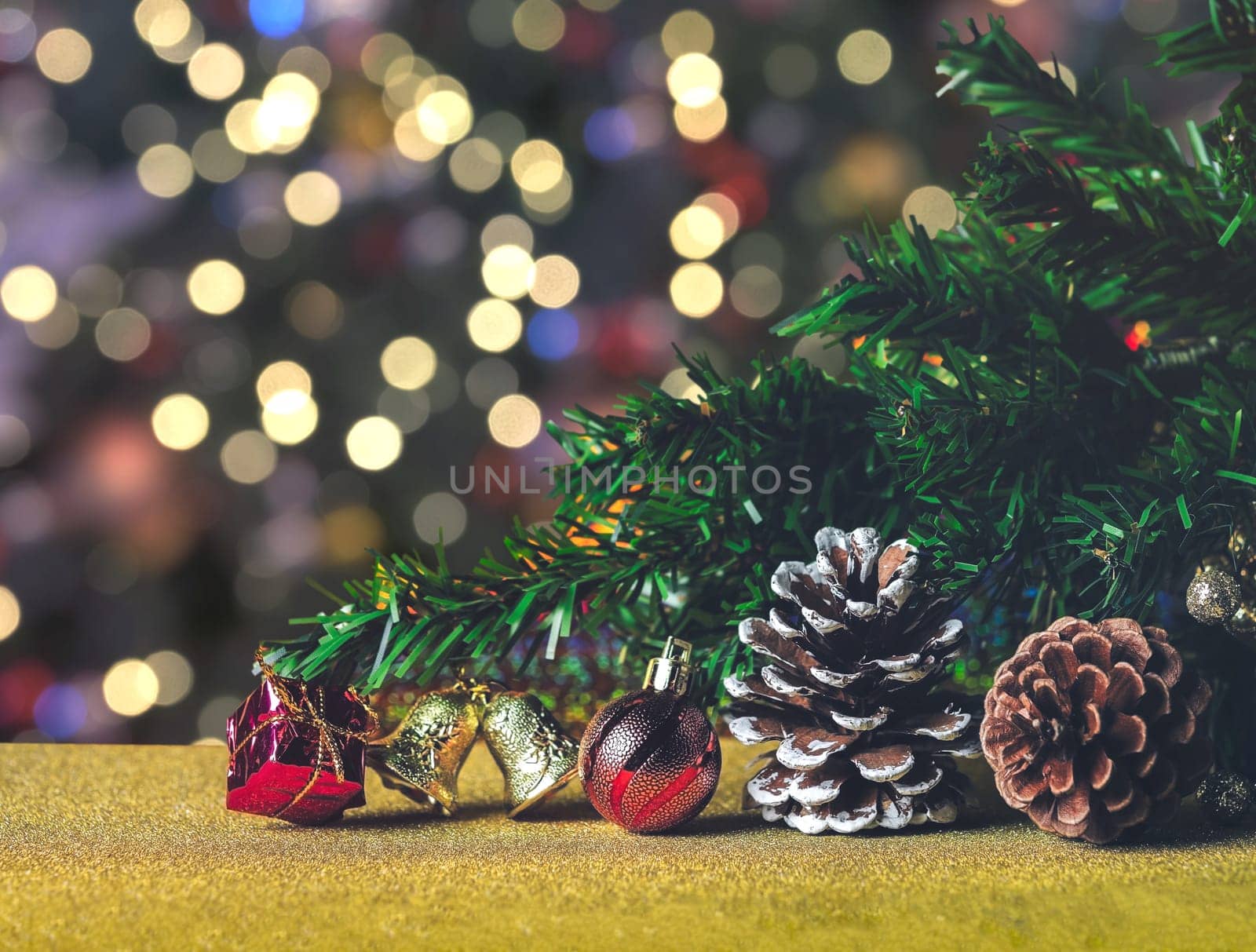 Branch of Christmas tree decoration with pinecones, red ball, gold bell and red gift box with bokeh lights background