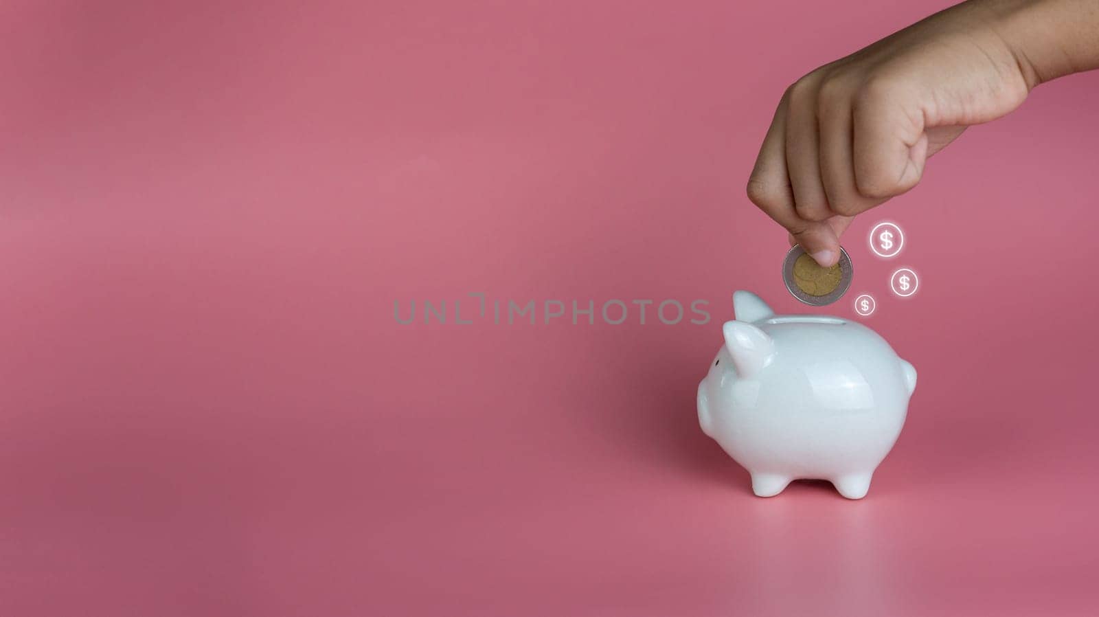 A human hand put a coin in a piggy bank on a pink background. Savings and investment concepts.