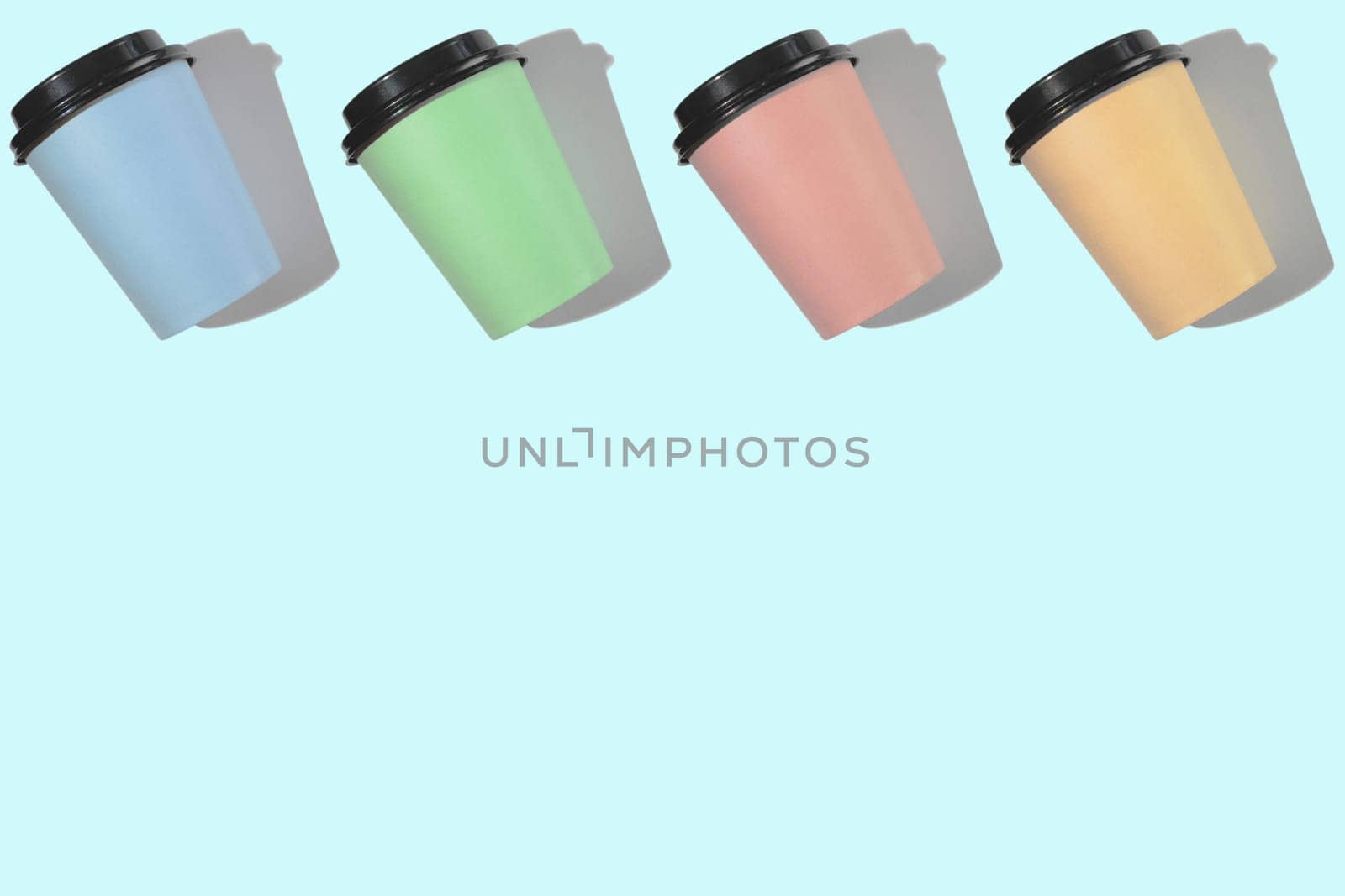 Four multi-colored cardboard coffee cups with a plastic lid on a blue background. Template with copy space. The concept of ecology, recycling, environmental protection.