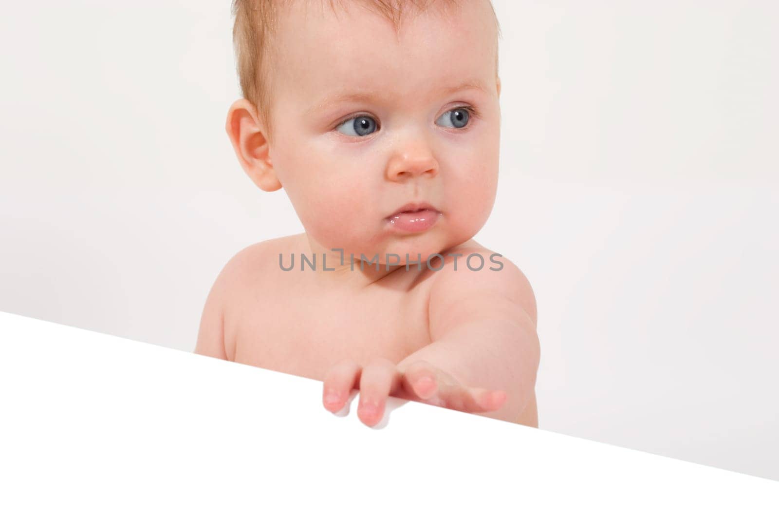 cute little baby looking into camera, holding a paper sheet