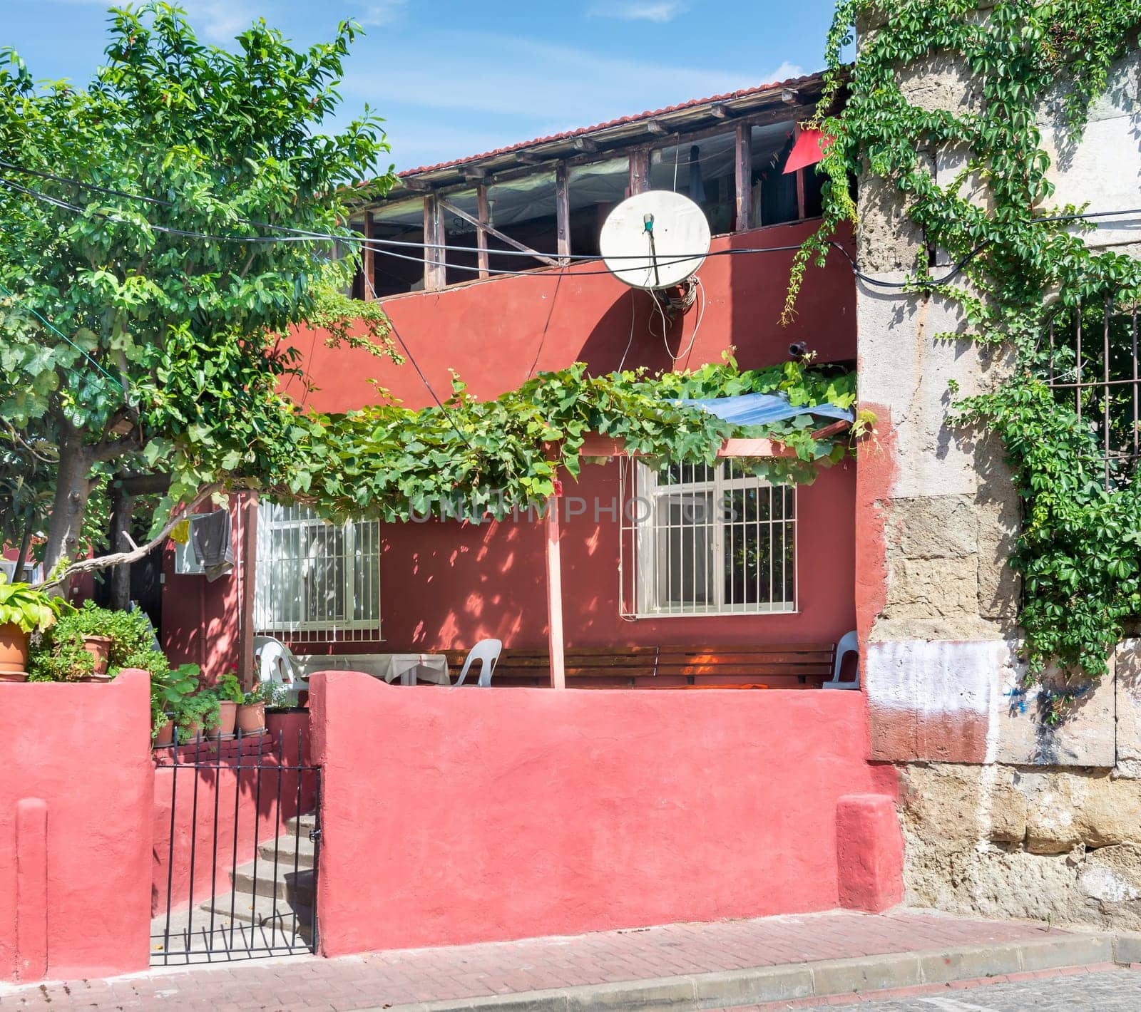 Exterior facade of old red painted traditional residential house, with wrought iron windows, climber plants, and green trees, Balat district, Istanbul, Turkey
