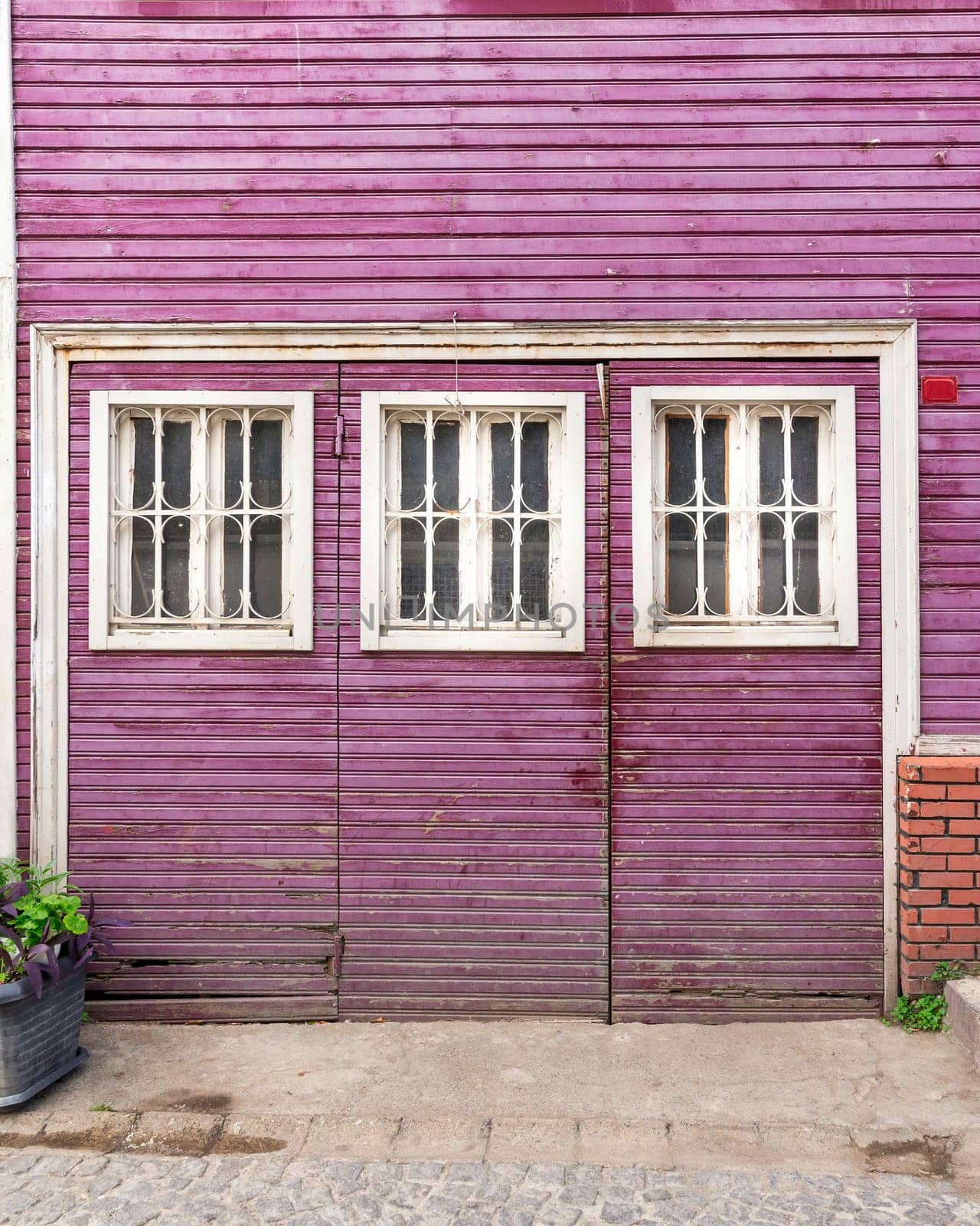 Wooden grunge weathered abandoned door painted in purple, with three white wooden windows painted in white, in a cobblestone alley
