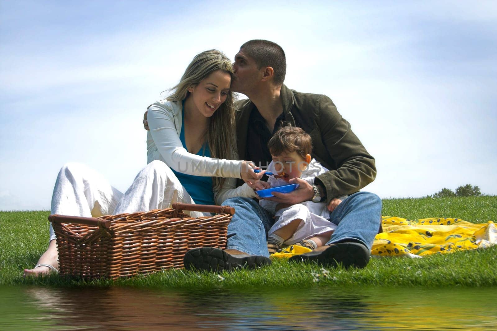 family outdoor in a field near water having a pick nick