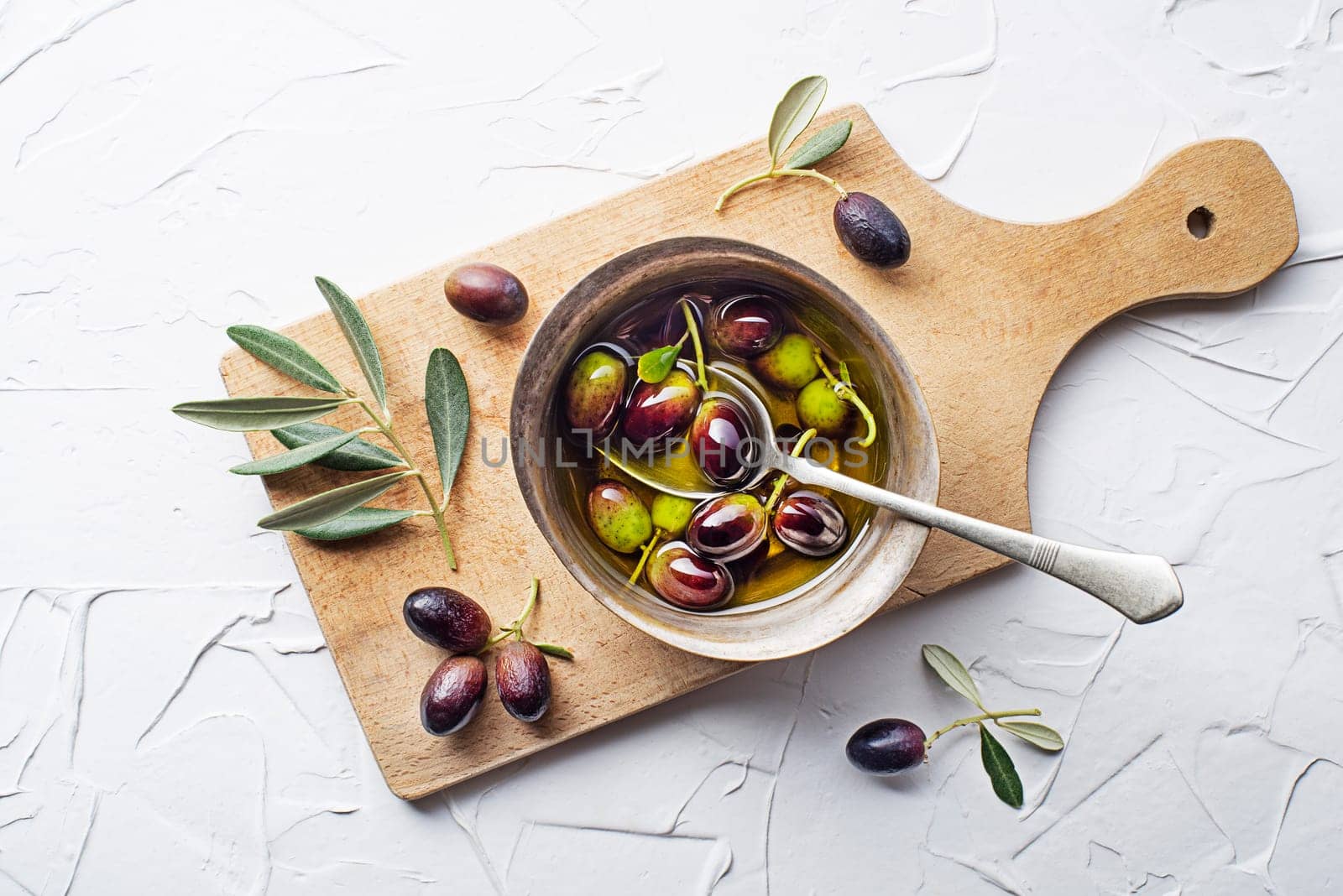 Olive oil in bowl with fresh olives fruit and olive branch on white background close up