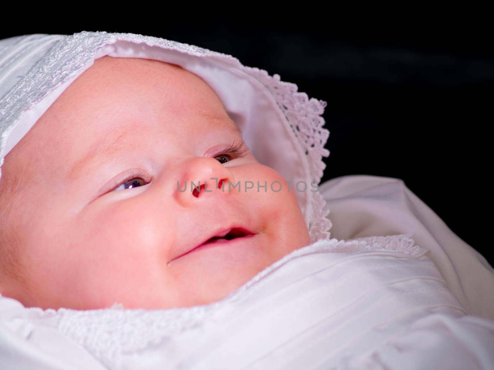 A close up on baby girl in a christening dress on a dark background.