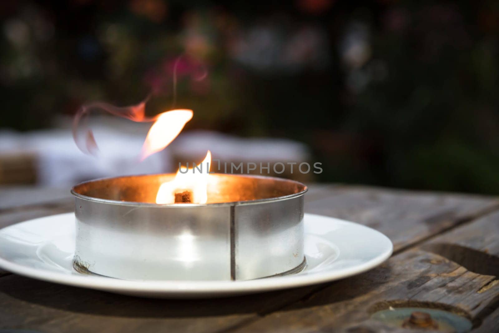 Burning decorative metal candle on blurred background.