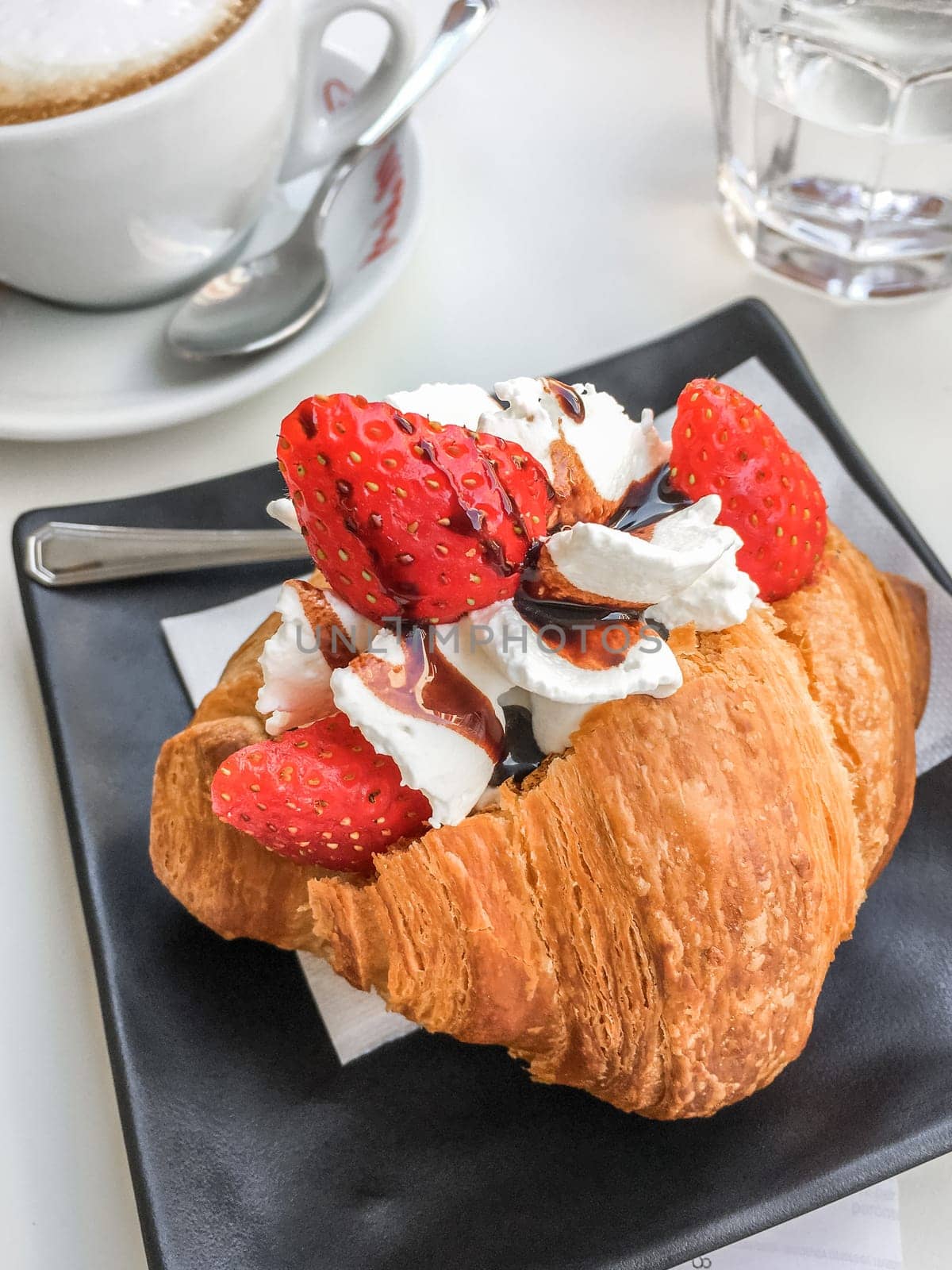 Italian breakfast. Croissant stuffed with whipped cream and strawberries and cappuccino.