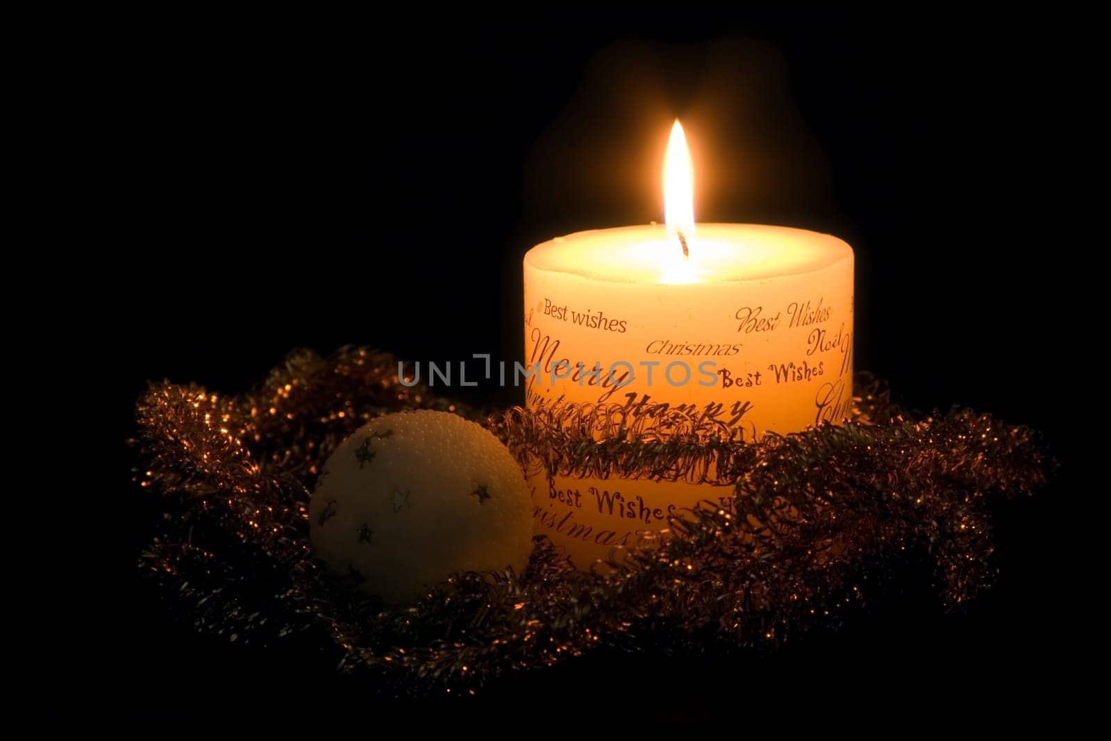 Lit white Christmas candle, golden ribbon and white christmas ball, on black background