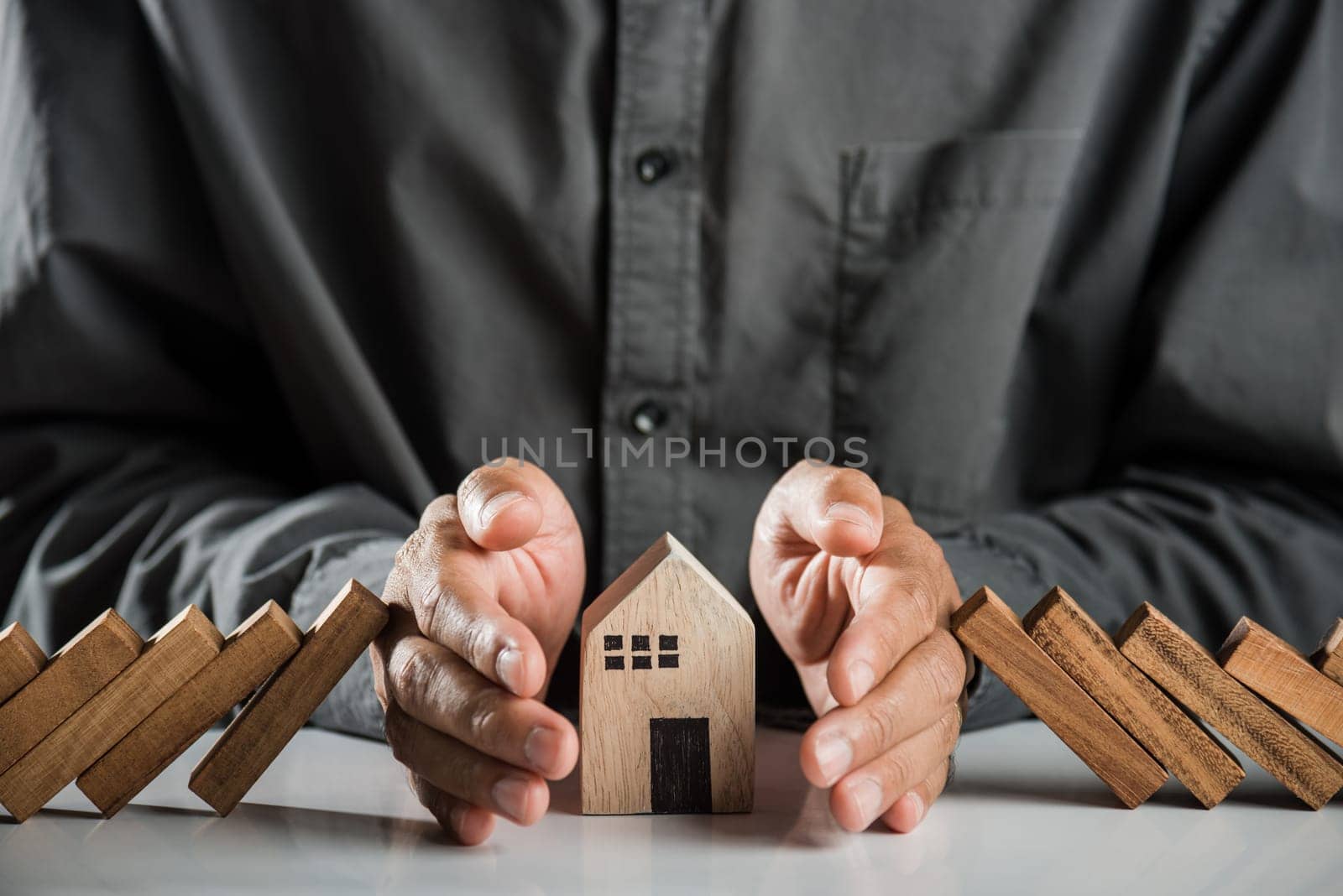 Business risk plan real estate protection. Man hand blocks wood block from many row falling wooden block like domino to house model, Insurance ideas to prevent loss concept