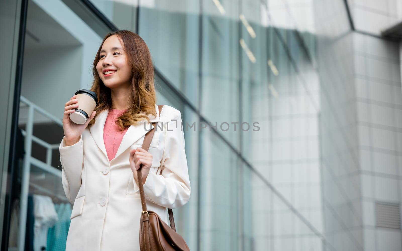 Happy business woman smiling hold paper cup of hot drink outdoor walking on street, Asian businesswoman holding coffee cup takeaway going to work she walking near her office building outside