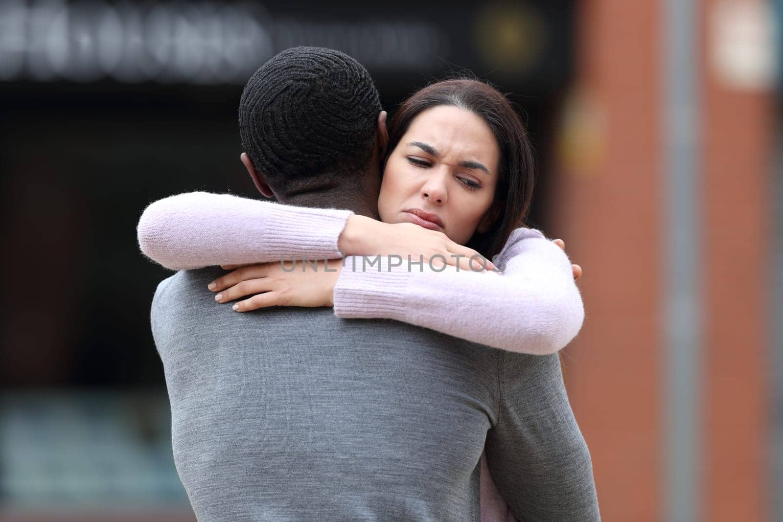 Disappointed woman hugging a black man in the street