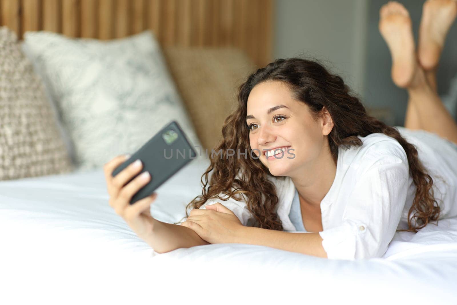 Happy woman lying on a bed taking selfie or recording video with phone