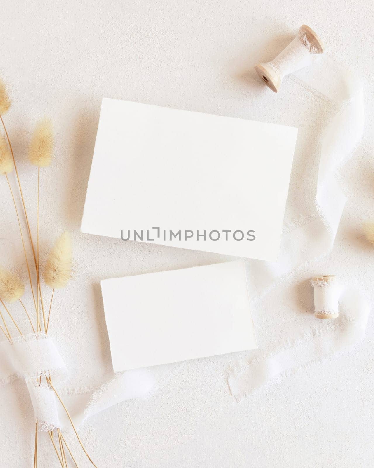 Blank cards near silk ribbons and dried hare's tail grass top view on white, mockup. Boho romantic scene with horizontal cards. Bohemian or close to nature greeting or wedding Invitation
